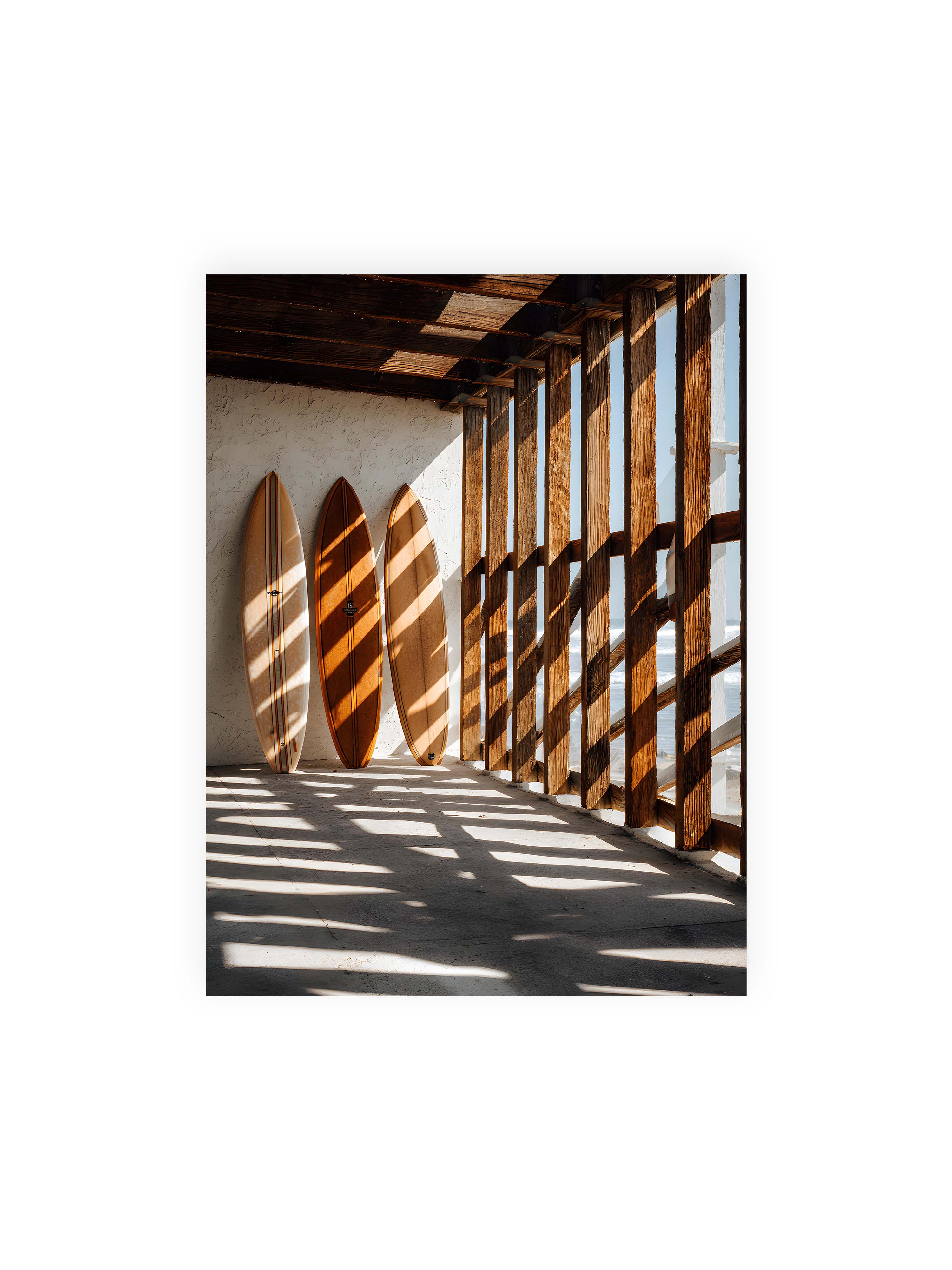 30x40 cm ohne Galerie-Rand ohne Rahmen – Drei Surfboards an einer hellen Wand, Holzpfosten werfen diagonale Schatten; Meer und Himmel schimmern im Hintergrund.