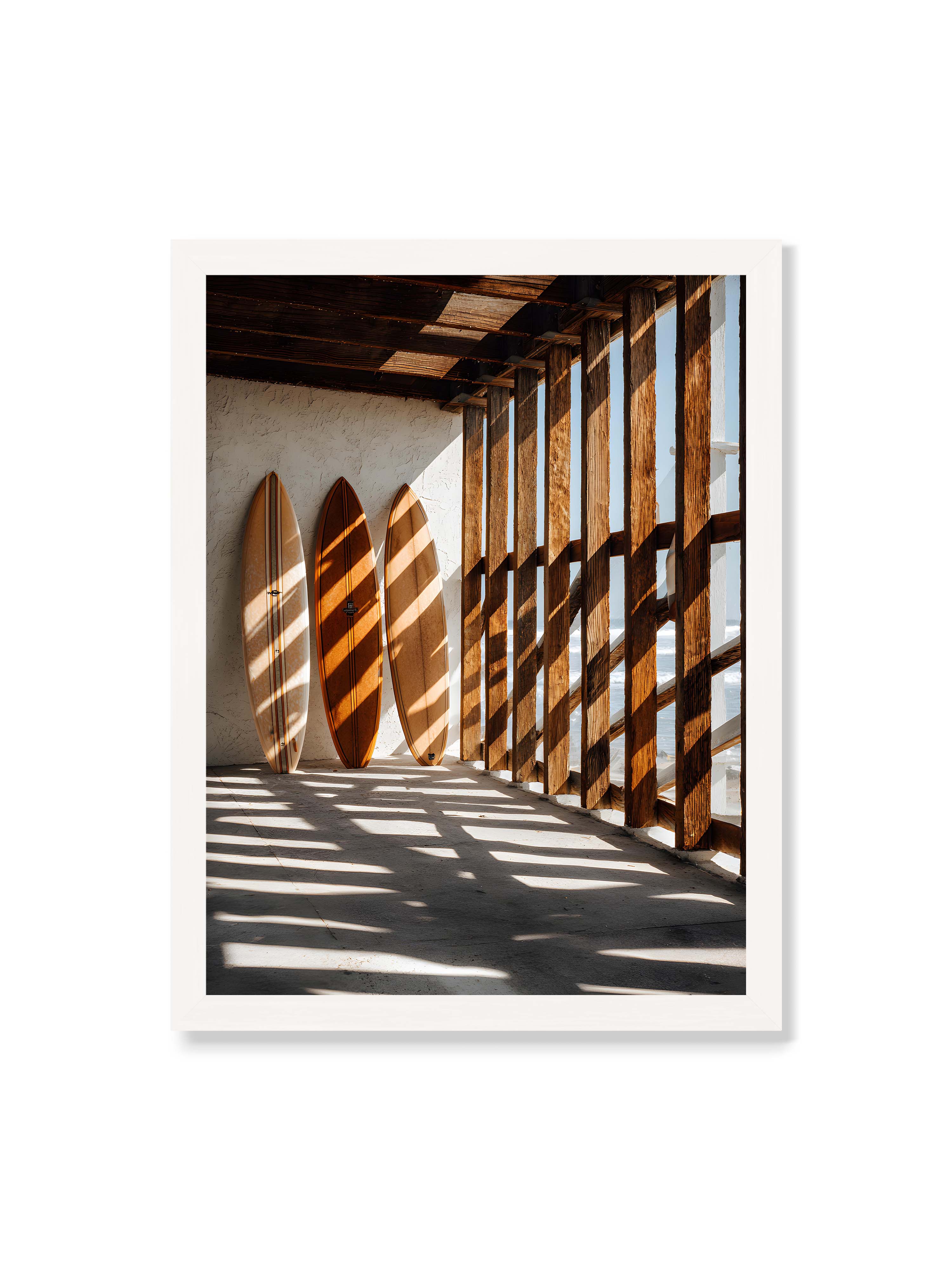 30x40 cm ohne Galerie-Rand mit weißem Rahmen – Drei Surfboards an einer hellen Wand, Holzpfosten werfen diagonale Schatten; Meer und Himmel schimmern im Hintergrund.