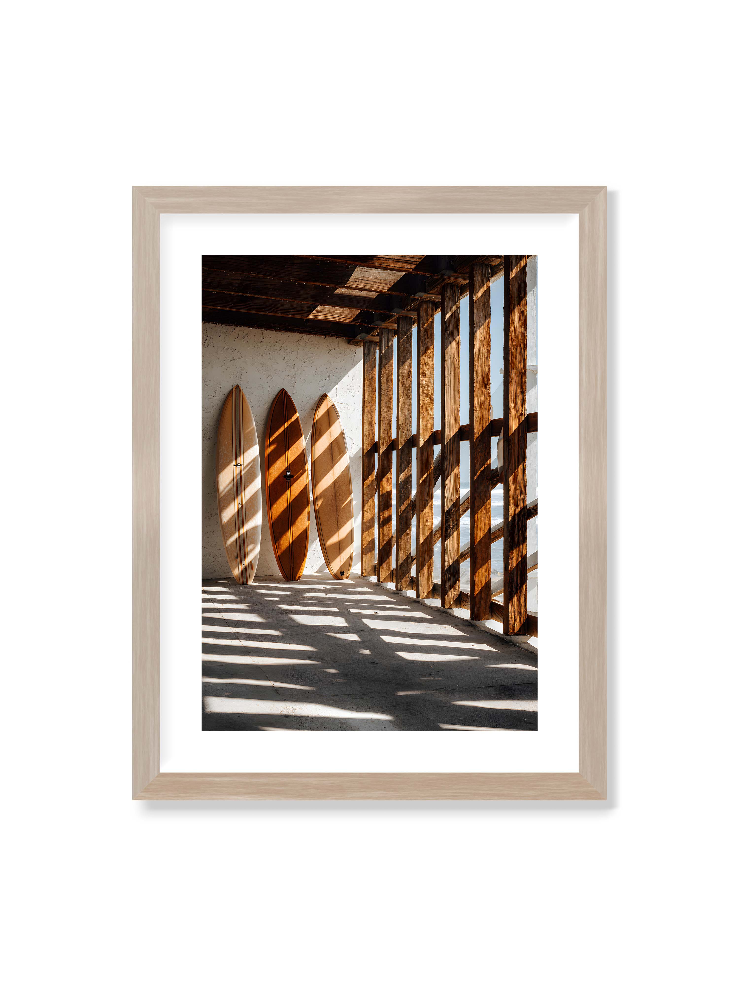 30x40 cm mit weißem Galerie-Rand im Eichenrahmen – Drei Surfboards an einer hellen Wand, Holzpfosten werfen diagonale Schatten; Meer und Himmel schimmern im Hintergrund.