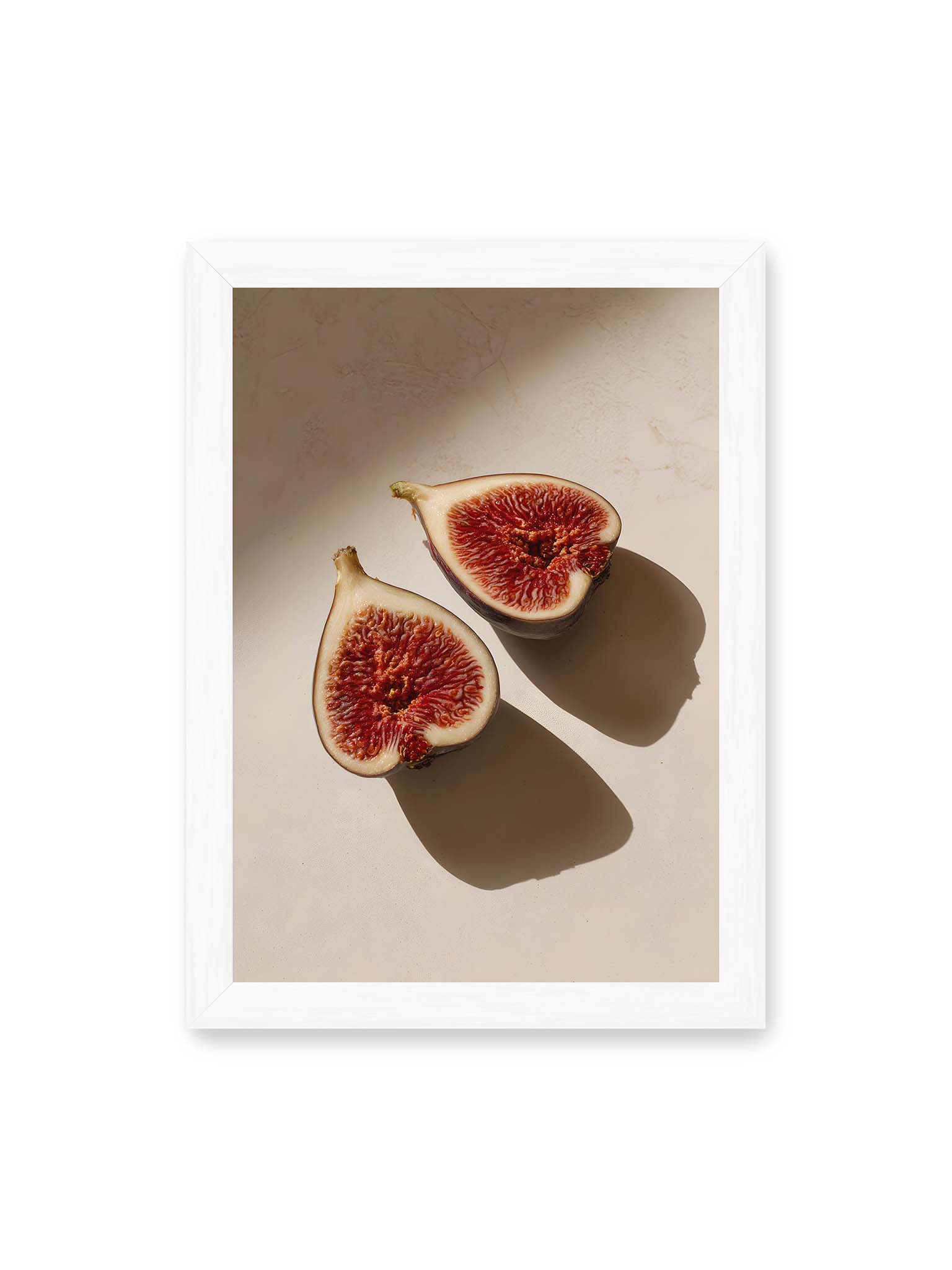 21x30 cm, weißer Rahmen – Halbierte Feigen auf heller Oberfläche mit warmem Licht und langen Schatten, sichtbar strukturierte rote Fruchtmitte.