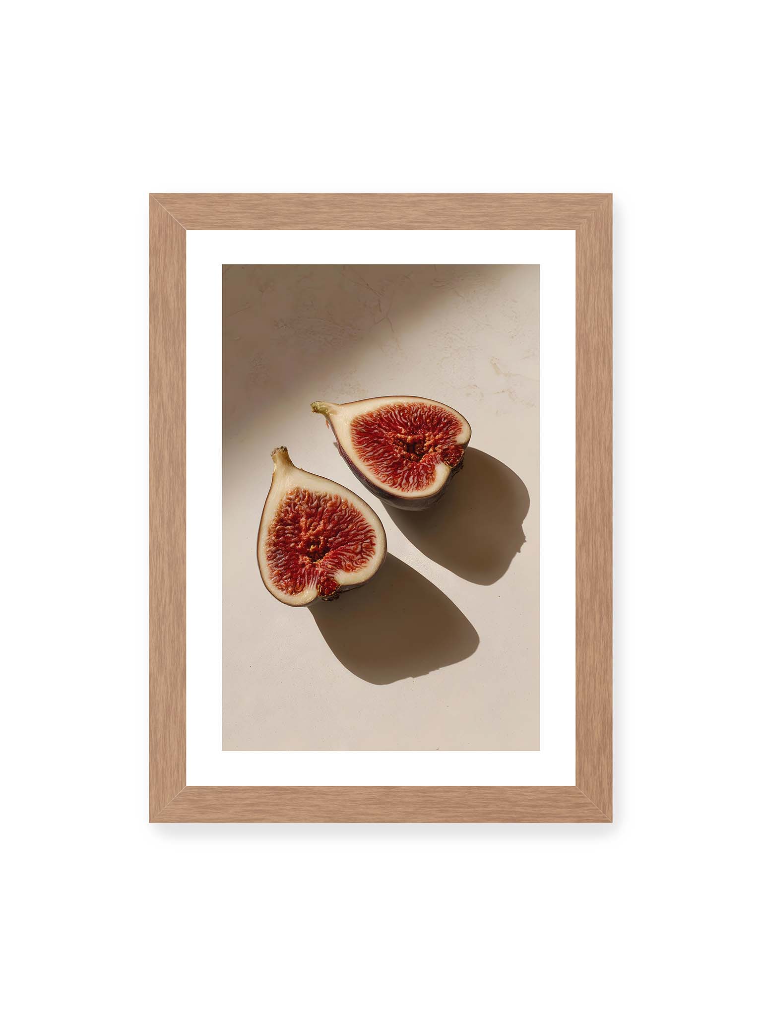 21x30 cm, weißer Galerie-Rand, Eichenrahmen – Halbierte Feigen auf heller Oberfläche mit warmem Licht und langen Schatten, sichtbar strukturierte rote Fruchtmitte.
