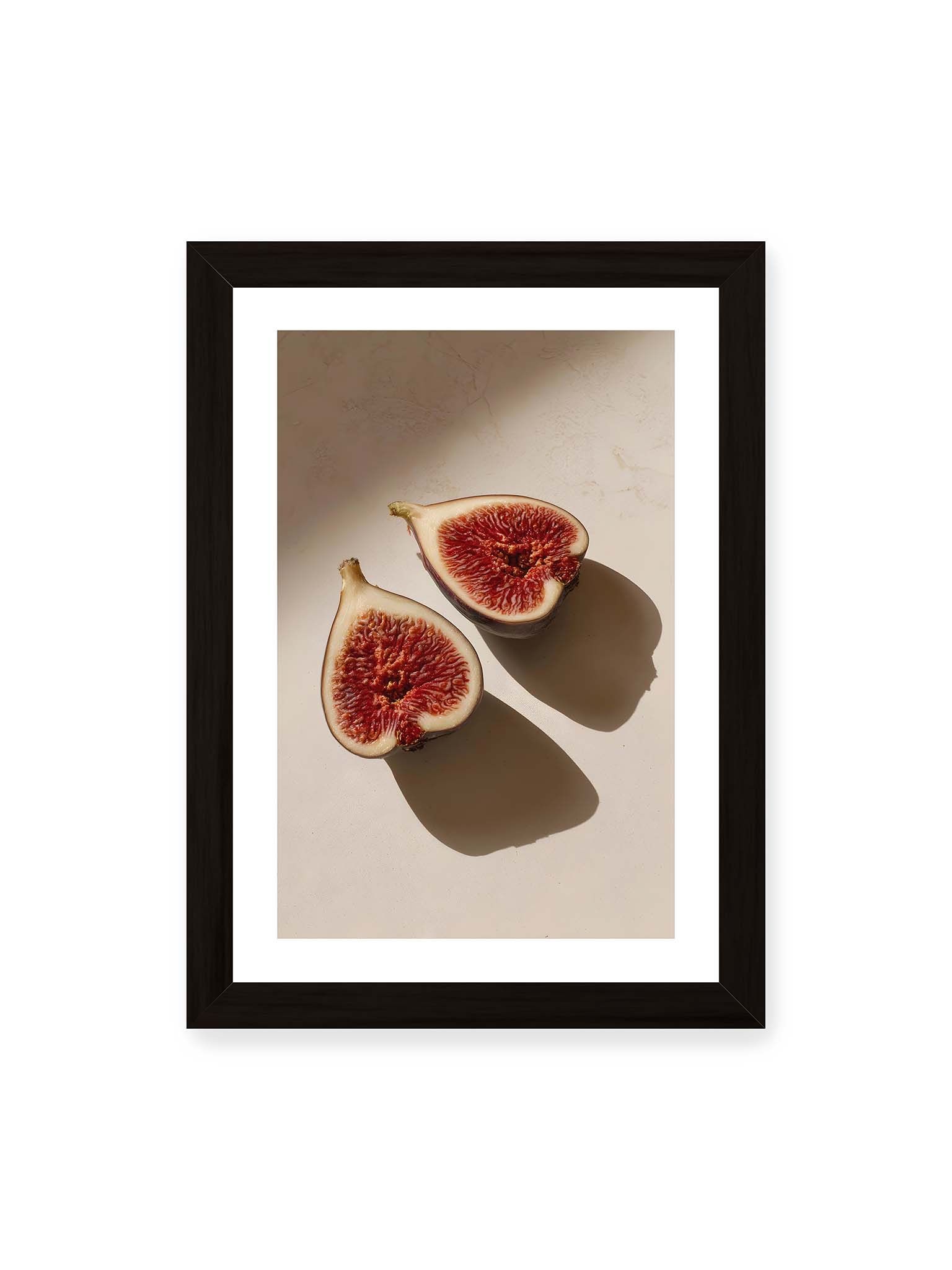 21x30 cm, weißer Galerie-Rand, schwarzer Rahmen – Halbierte Feigen auf heller Oberfläche mit warmem Licht und langen Schatten, sichtbar strukturierte rote Fruchtmitte.