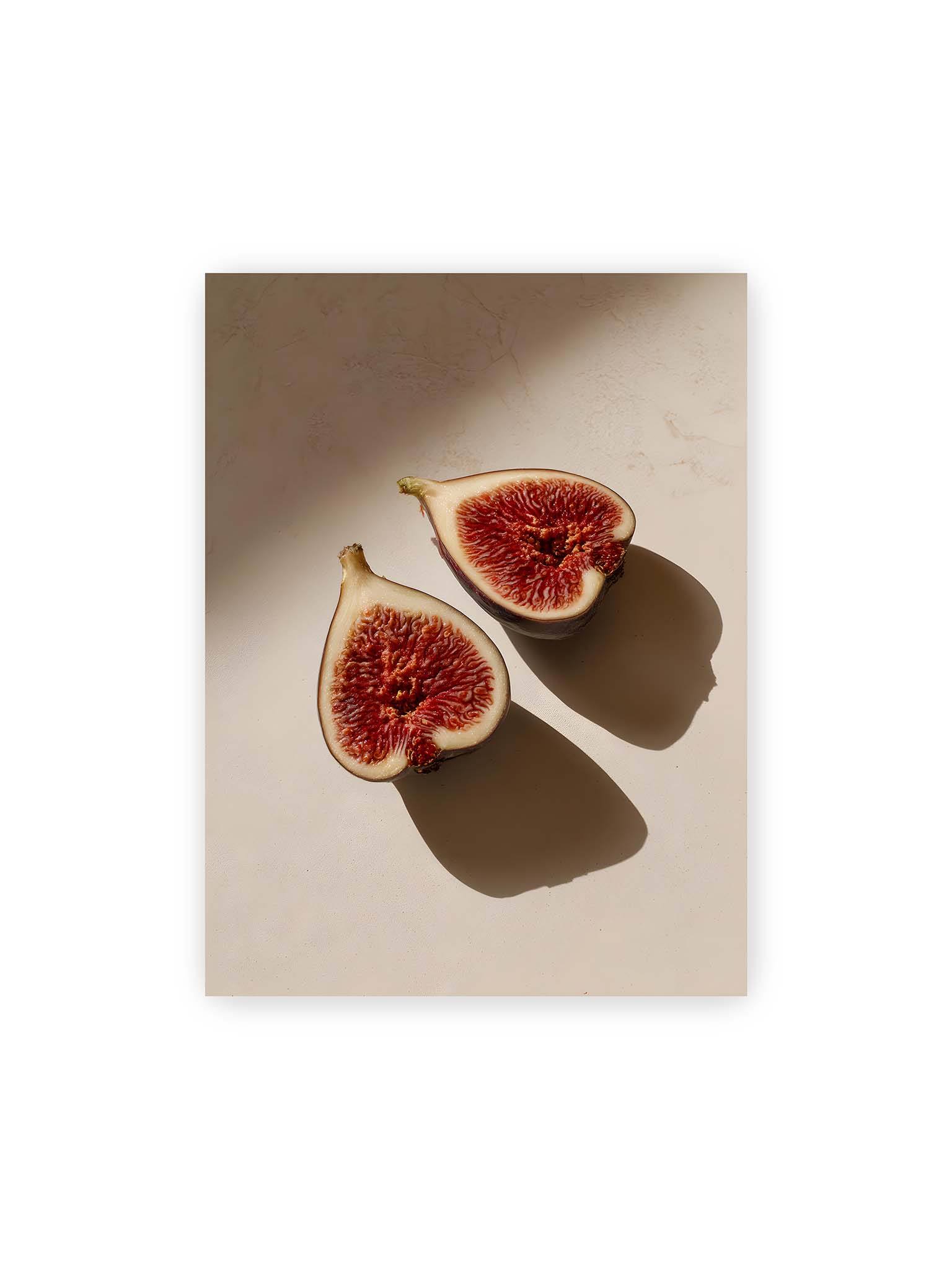 30x40 cm – Halbierte Feigen auf heller Oberfläche mit warmem Licht und langen Schatten, sichtbar strukturierte rote Fruchtmitte.