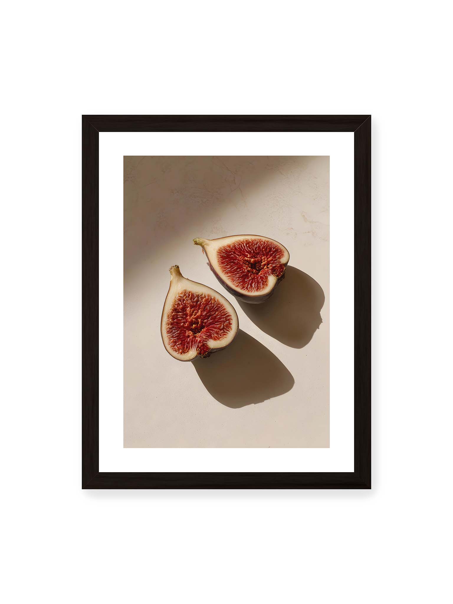30x40 cm, weißer Galerie-Rand, schwarzer Rahmen – Halbierte Feigen auf heller Oberfläche mit warmem Licht und langen Schatten, sichtbar strukturierte rote Fruchtmitte.