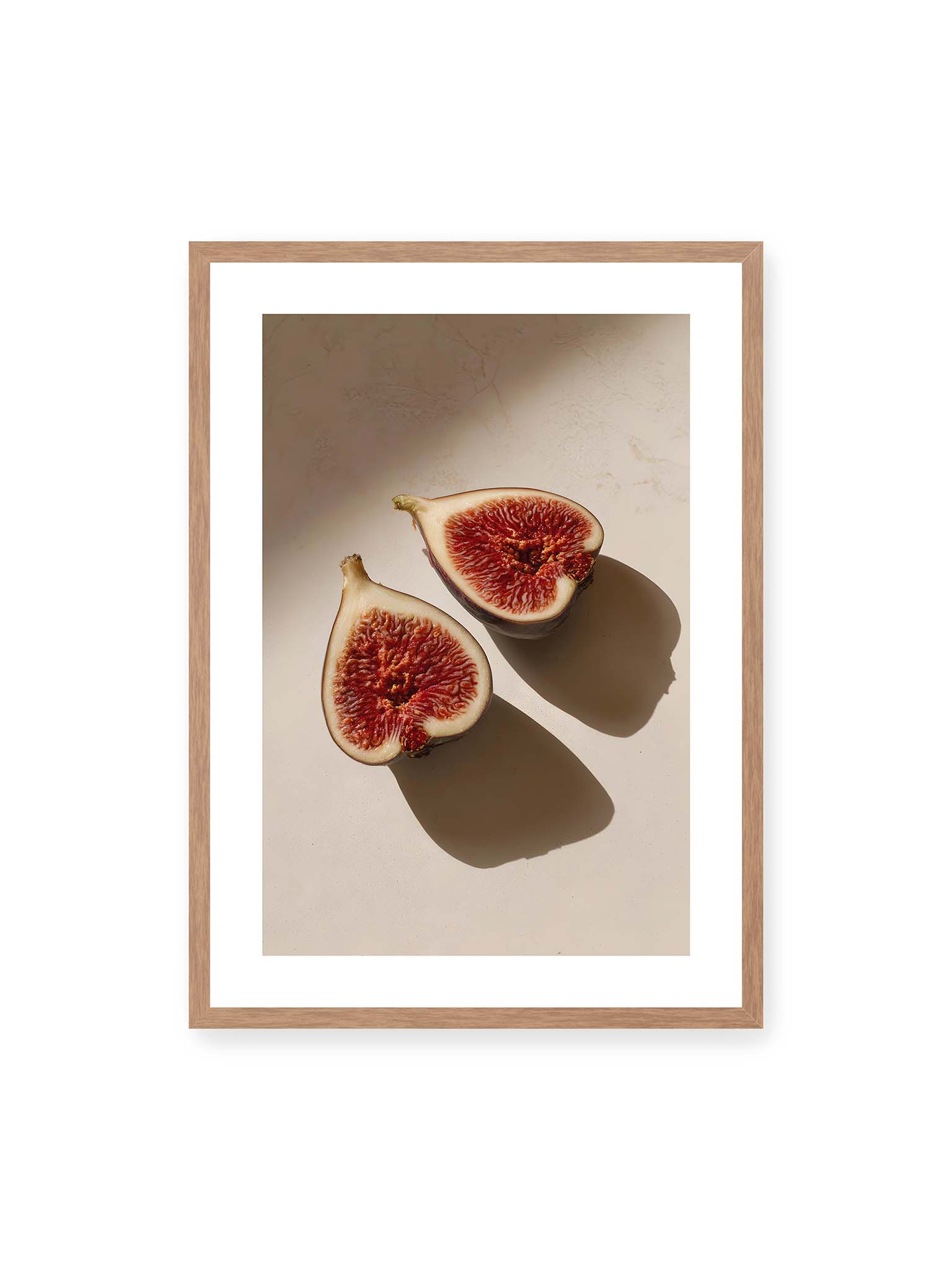 50x70 cm, weißer Galerie-Rand, Eichenrahmen – Halbierte Feigen auf heller Oberfläche mit warmem Licht und langen Schatten, sichtbar strukturierte rote Fruchtmitte.