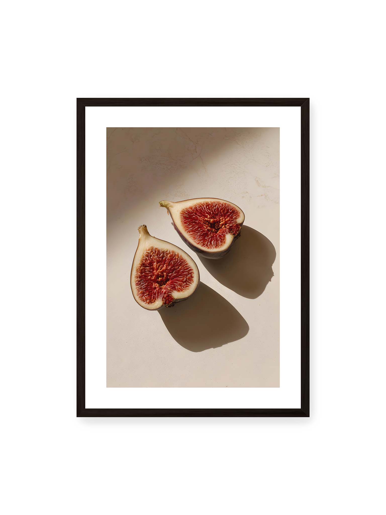 50x70 cm, weißer Galerie-Rand, schwarzer Rahmen – Halbierte Feigen auf heller Oberfläche mit warmem Licht und langen Schatten, sichtbar strukturierte rote Fruchtmitte.