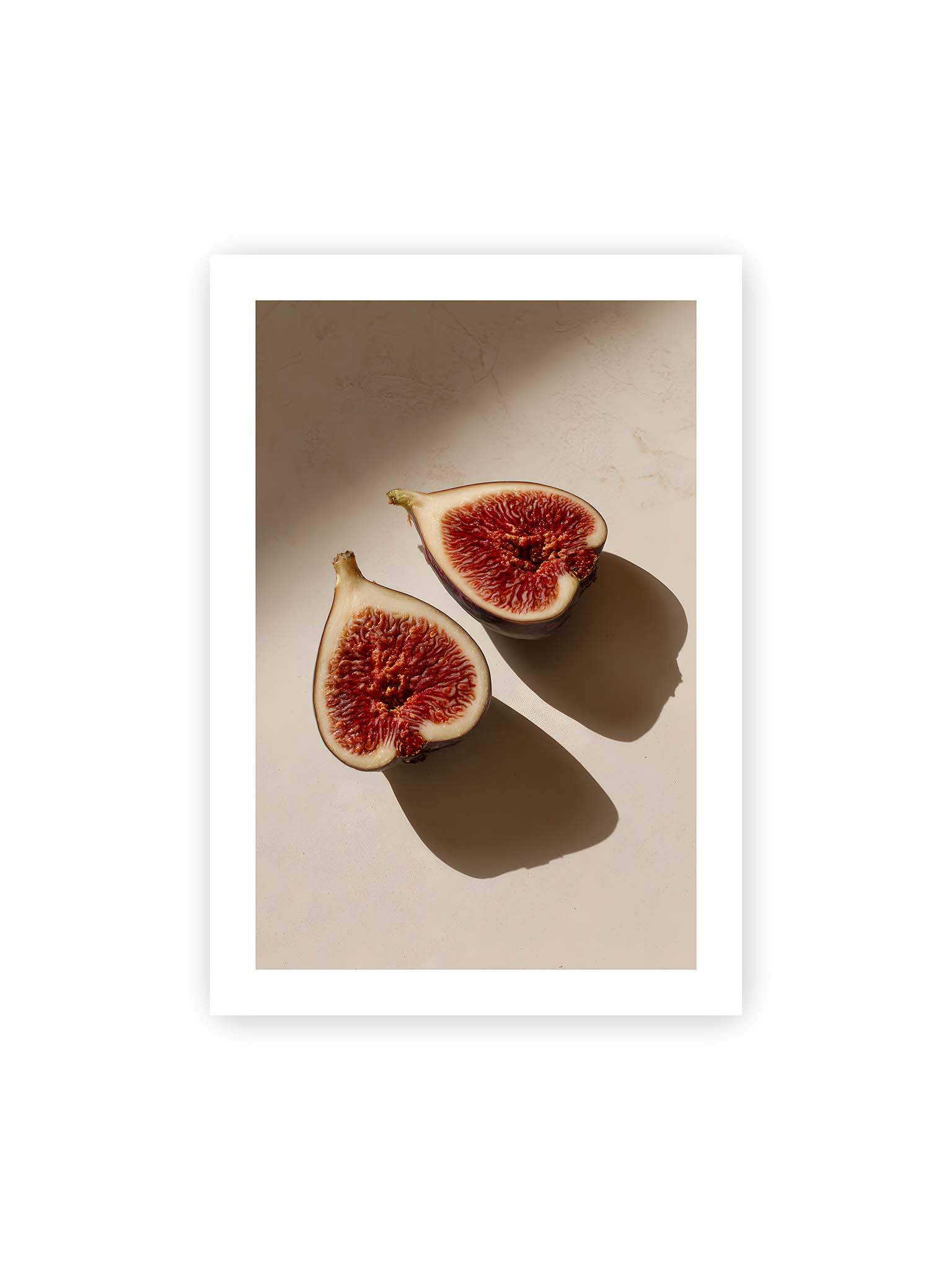 70x100 cm, weißer Galerie-Rand – Halbierte Feigen auf heller Oberfläche mit warmem Licht und langen Schatten, sichtbar strukturierte rote Fruchtmitte.