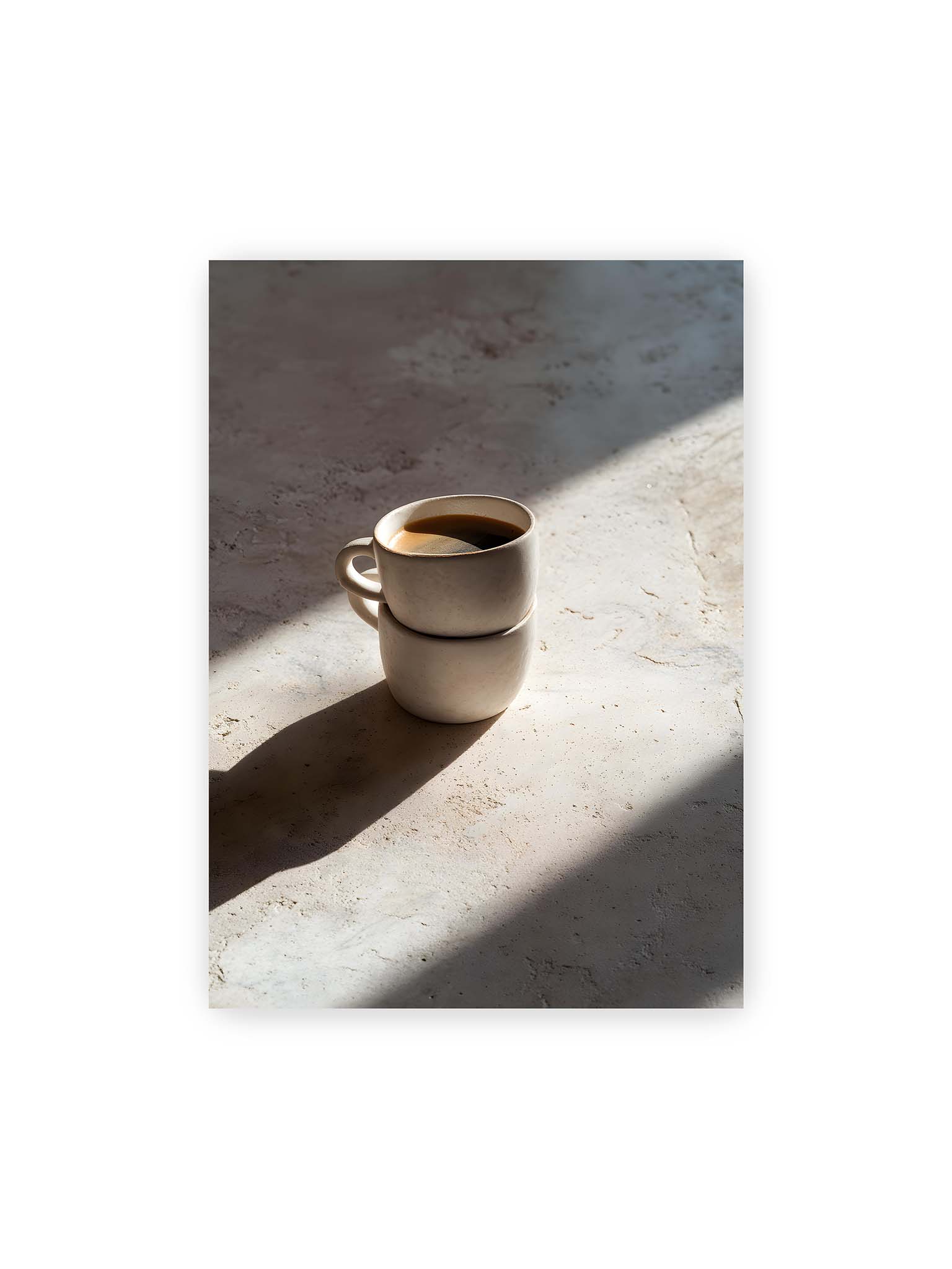 50x70 cm – Zwei gestapelte Keramiktassen mit schwarzem Kaffee auf heller Oberfläche, beleuchtet von schrägem Morgenlicht mit langen Schatten.
