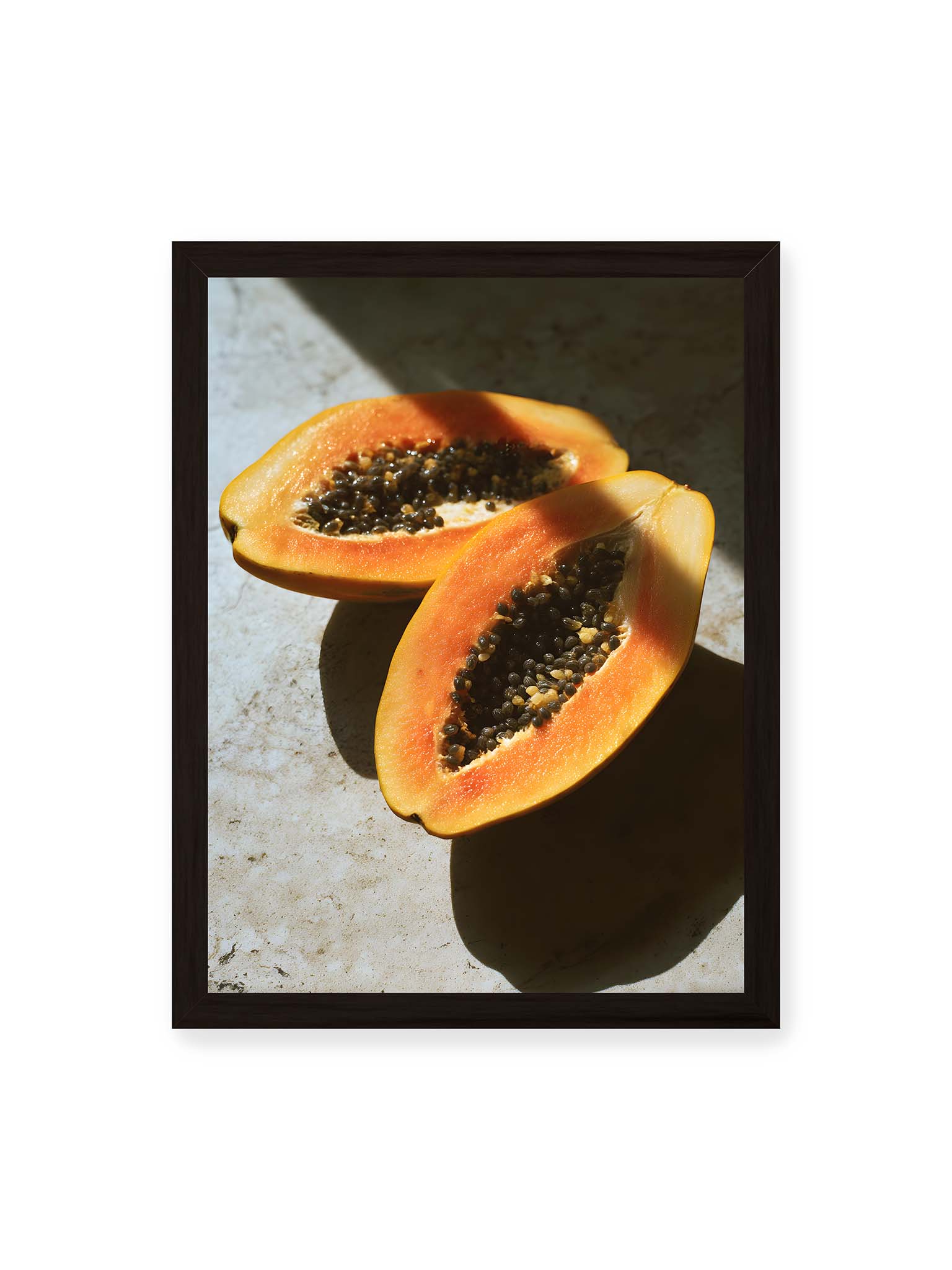 30x40 cm, schwarzer Rahmen – Zwei halbierte Papayas mit dunklen Samen auf heller Oberfläche, beleuchtet von warmem Licht mit starken Schatten.