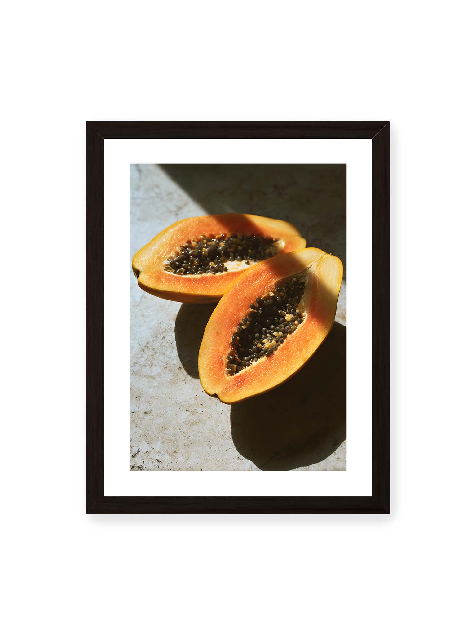 30x40 cm, weißer Galerie-Rand, schwarzer Rahmen – Zwei halbierte Papayas mit dunklen Samen auf heller Oberfläche, beleuchtet von warmem Licht mit starken Schatten.