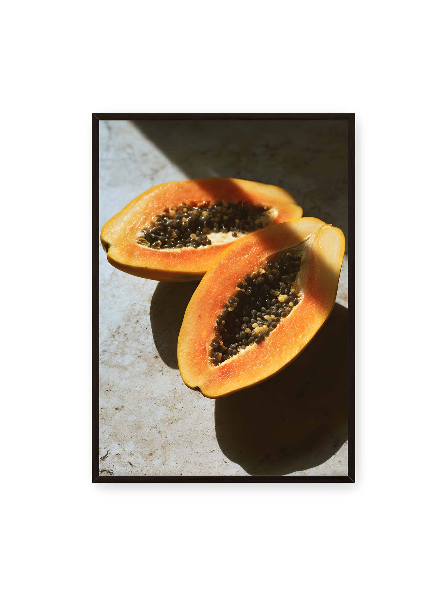 70x100 cm, schwarzer Rahmen – Zwei halbierte Papayas mit dunklen Samen auf heller Oberfläche, beleuchtet von warmem Licht mit starken Schatten.