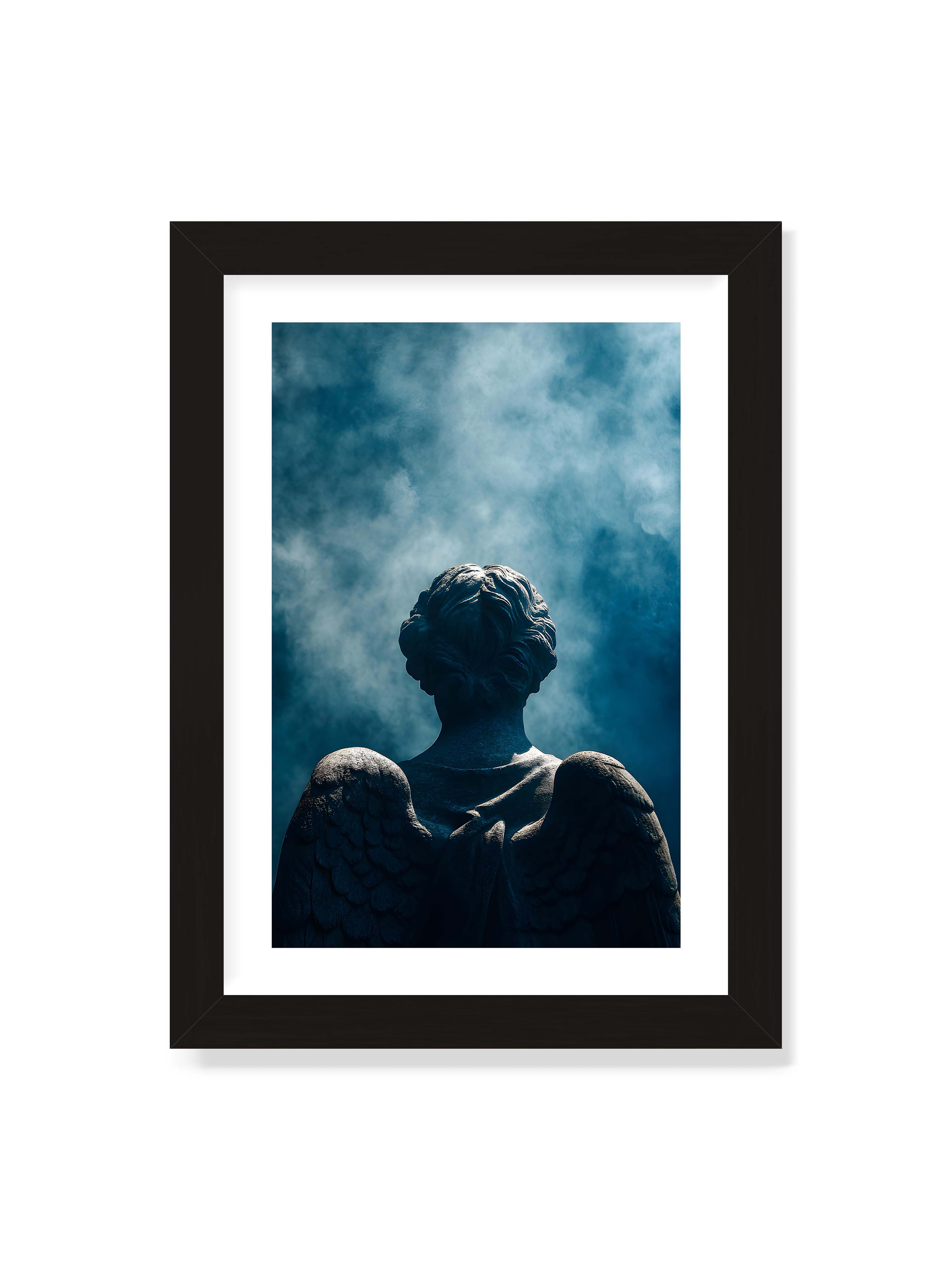 21x30 cm mit weißem Galerie-Rand mit schwarzem Rahmen – Steinerne Engelsfigur von hinten mit ausgebreiteten Flügeln vor blauem, nebligem Himmel.