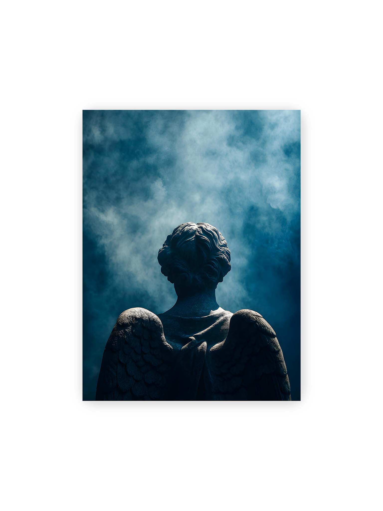 30x40 cm – Rückansicht einer steinernen Engelsfigur mit ausgebreiteten Flügeln vor blauem Himmel und aufsteigendem Nebel.