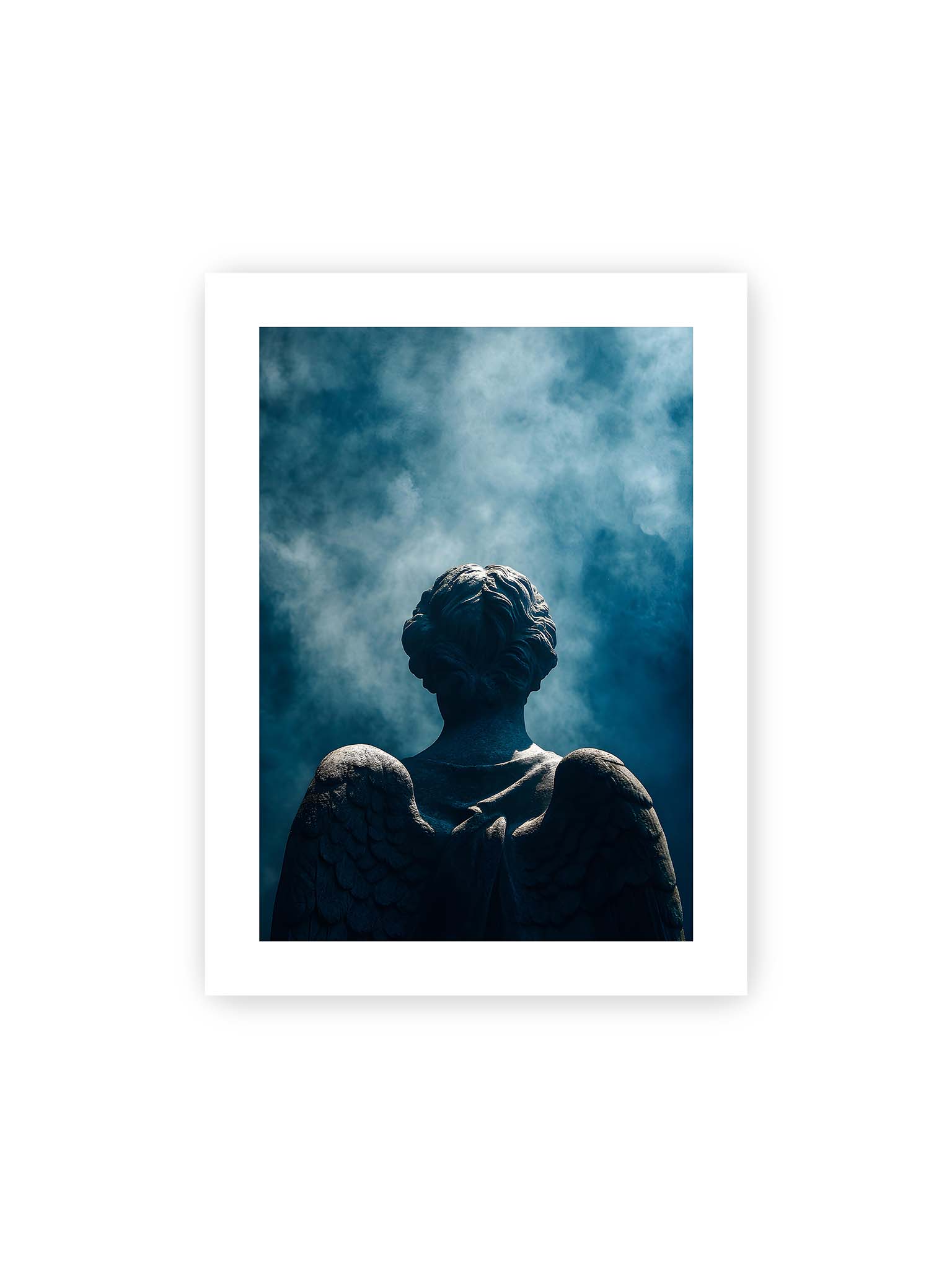 30x40 cm, weißer Galerie-Rand – Rückansicht einer steinernen Engelsfigur mit ausgebreiteten Flügeln vor blauem Himmel und aufsteigendem Nebel.