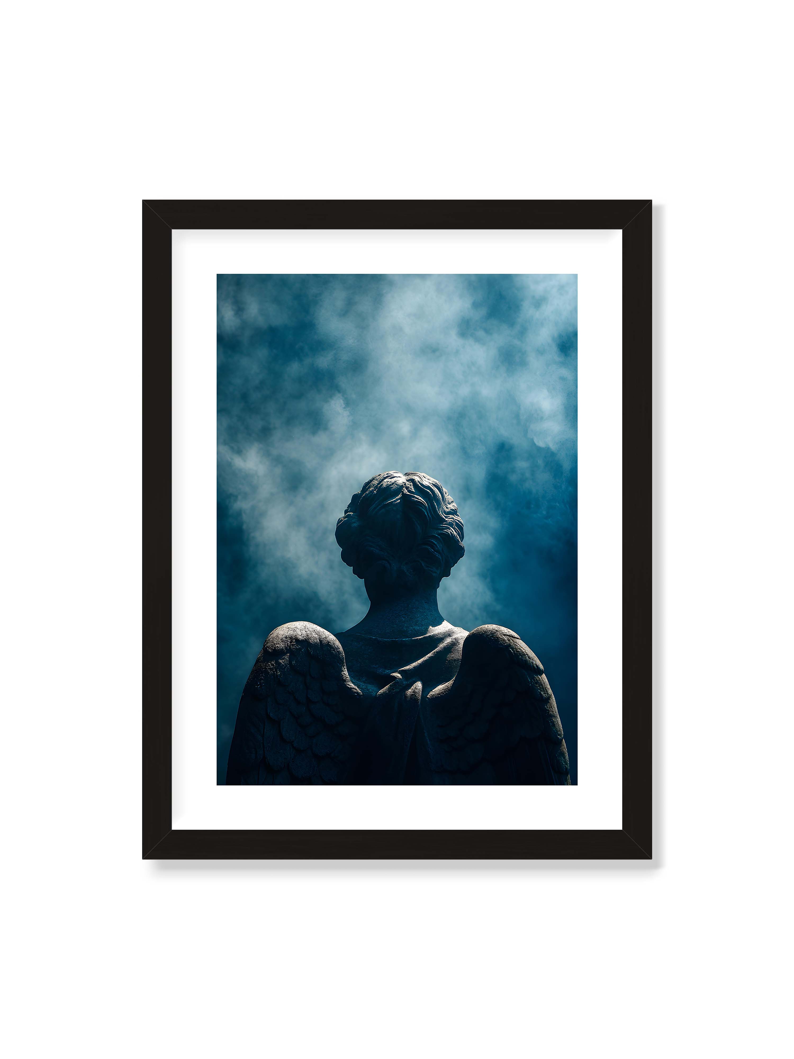 30x40 cm mit weißem Galerie-Rand mit schwarzem Rahmen – Steinerne Engelsfigur von hinten mit ausgebreiteten Flügeln vor blauem, nebligem Himmel.