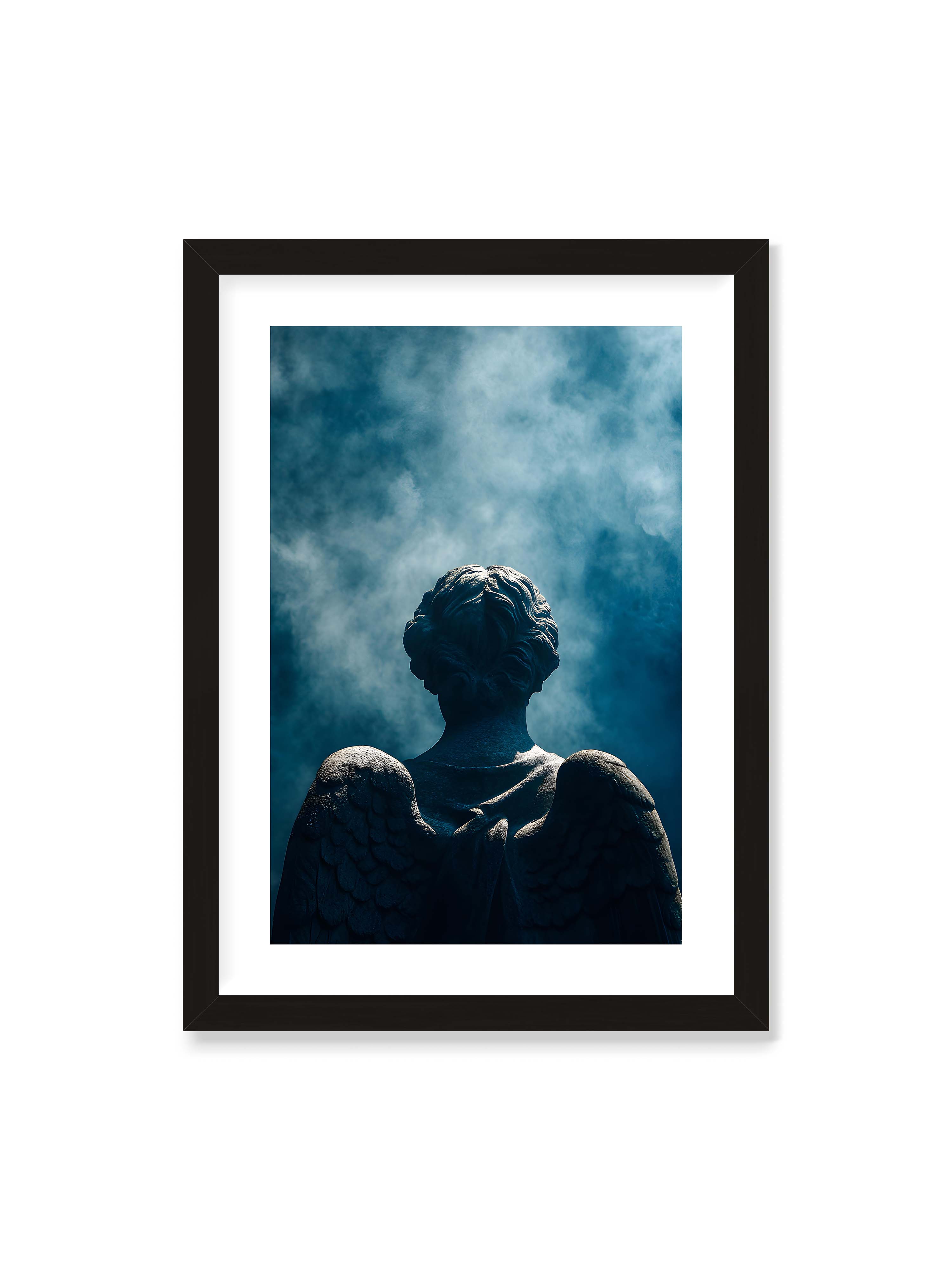 50x70 cm mit weißem Galerie-Rand mit schwarzem Rahmen – Steinerne Engelsfigur von hinten mit ausgebreiteten Flügeln vor blauem, nebligem Himmel.