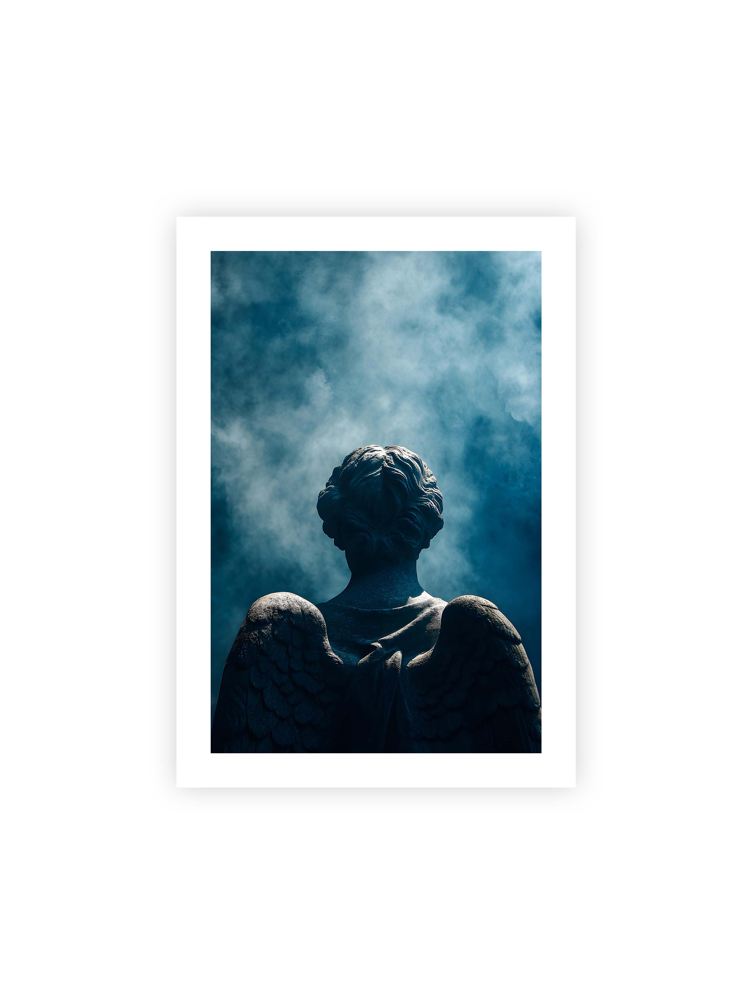 70x100 cm mit weißem Galerie-Rand ohne Rahmen – Steinerne Engelsfigur von hinten mit ausgebreiteten Flügeln vor blauem, nebligem Himmel.