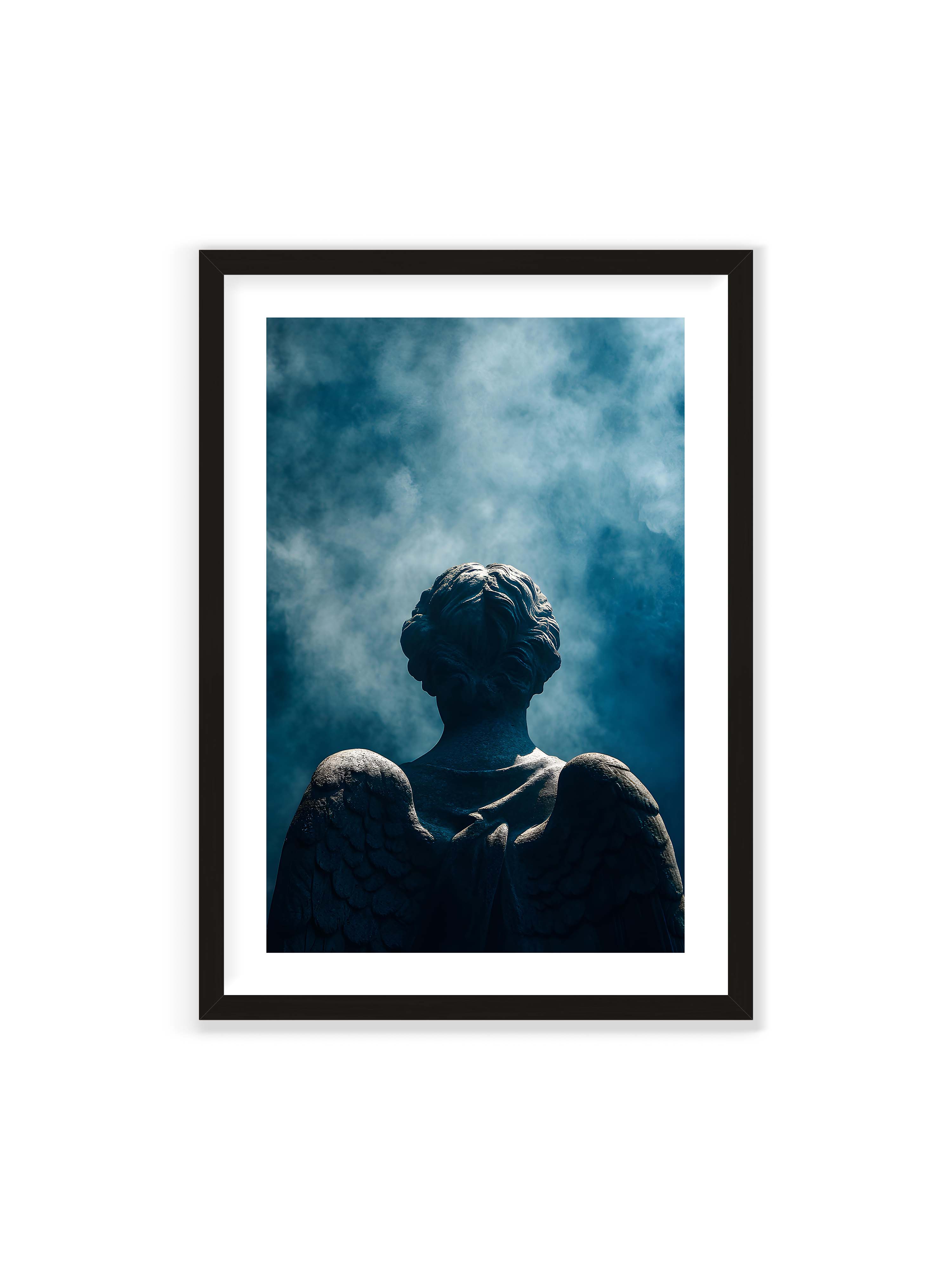 70x100 cm mit weißem Galerie-Rand mit schwarzem Rahmen – Steinerne Engelsfigur von hinten mit ausgebreiteten Flügeln vor blauem, nebligem Himmel.