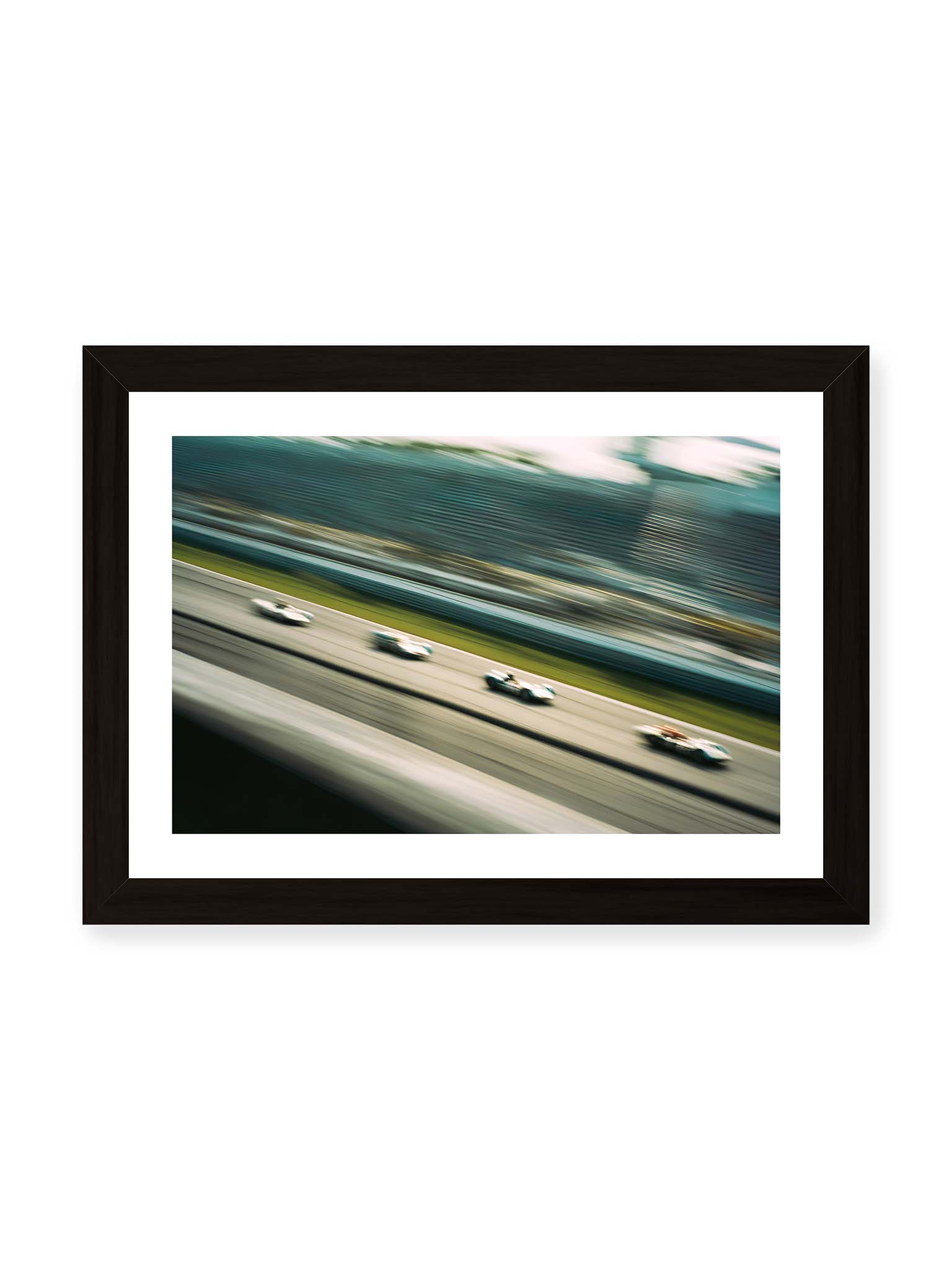 21x30 cm, weißer Galerie-Rand, schwarzer Rahmen – Mehrere Rennwagen in starker Bewegungsunschärfe auf einer Rennstrecke, diagonal ausgerichtet.