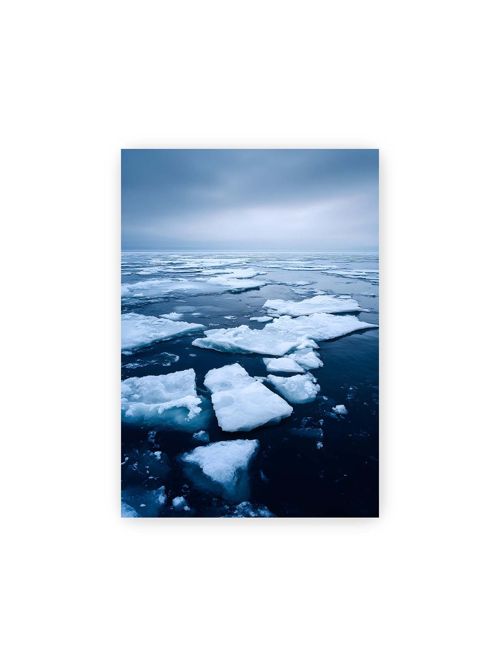 21x30 cm – Zerbrochene Eisschollen treiben auf dunklem Wasser unter bewölktem Himmel.