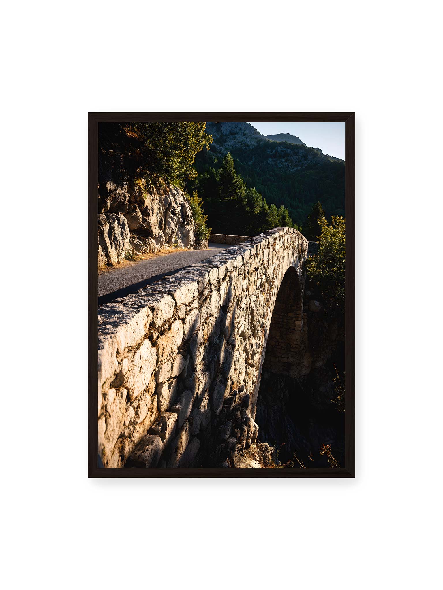 50x70 cm, schwarzer Rahmen – Steinbrücke mit architektonischem Bogen, beleuchtet vom Abendlicht, umrahmt von einer grünen Landschaft.