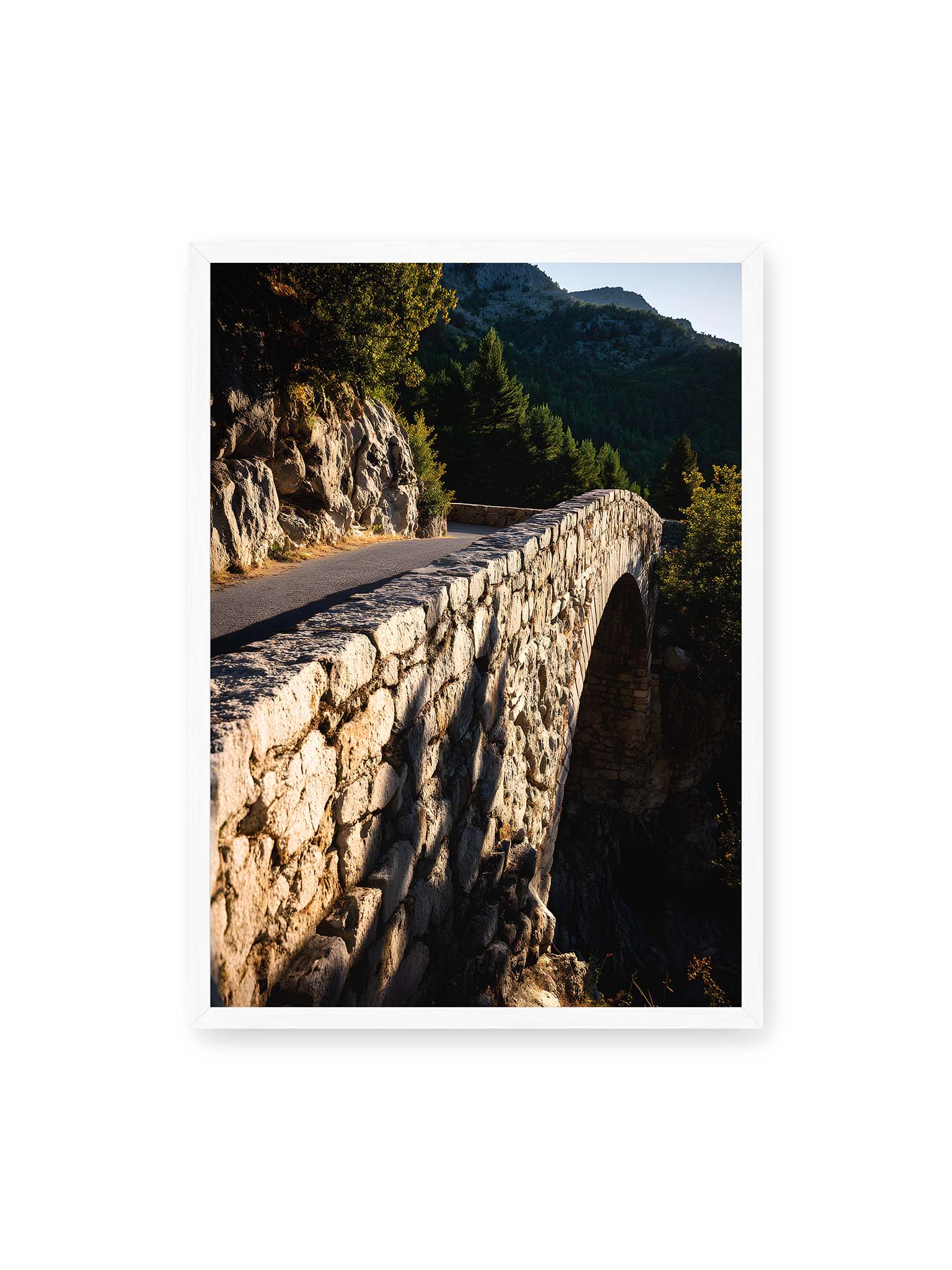 50x70 cm, weißer Rahmen – Steinbrücke mit architektonischem Bogen, beleuchtet vom Abendlicht, umrahmt von einer grünen Landschaft.