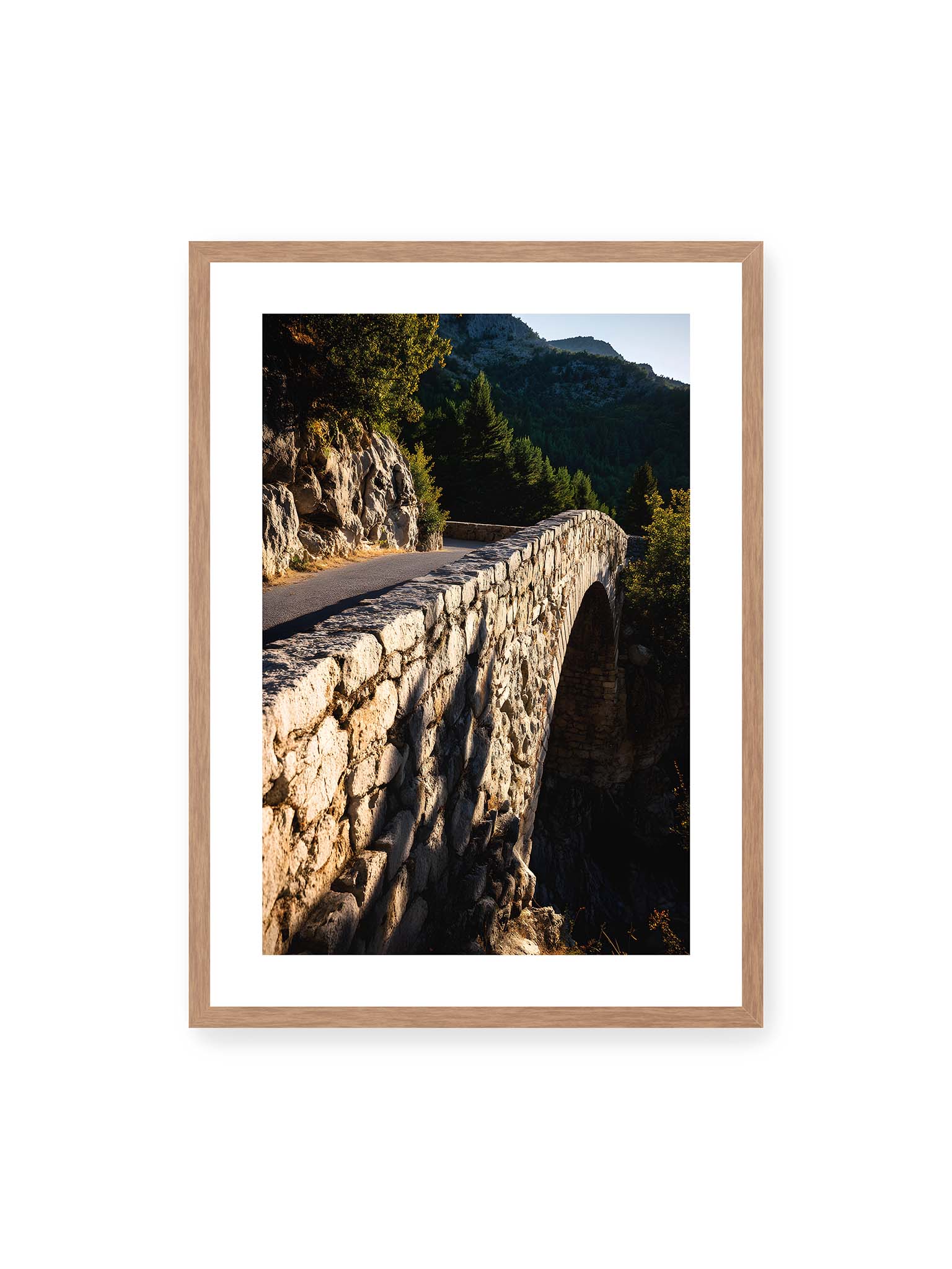 50x70 cm, weißer Galerie-Rand, Eichenrahmen – Steinbrücke mit architektonischem Bogen, beleuchtet vom Abendlicht, umrahmt von einer grünen Landschaft.