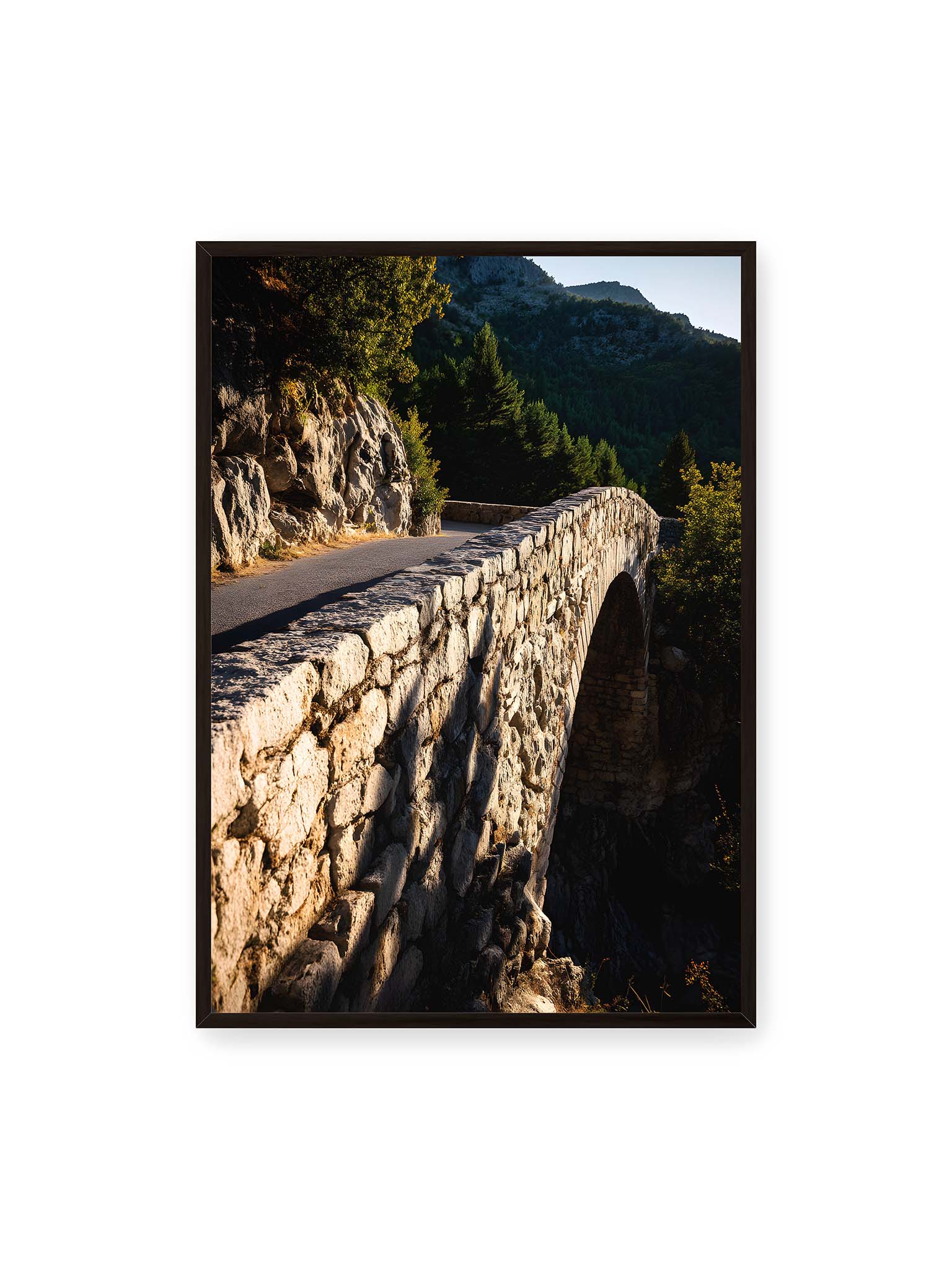 70x100 cm, schwarzer Rahmen – Steinbrücke mit architektonischem Bogen, beleuchtet vom Abendlicht, umrahmt von einer grünen Landschaft.