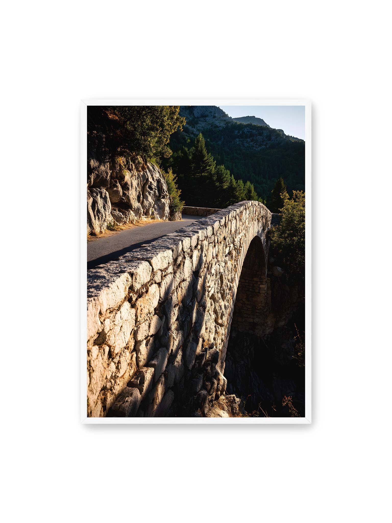 70x100 cm, weißer Rahmen – Steinbrücke mit architektonischem Bogen, beleuchtet vom Abendlicht, umrahmt von einer grünen Landschaft.