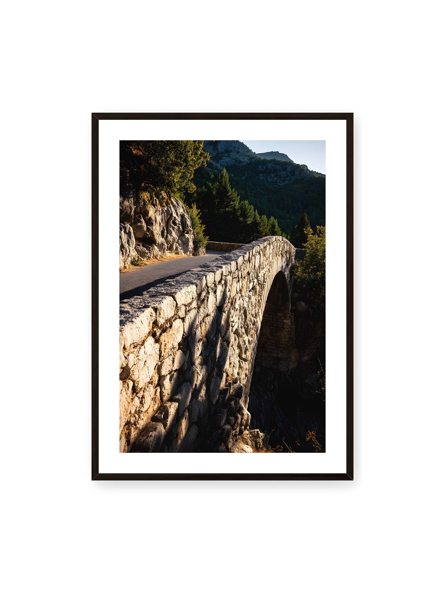 70x100 cm, weißer Galerie-Rand, schwarzer Rahmen – Steinbrücke mit architektonischem Bogen, beleuchtet vom Abendlicht, umrahmt von einer grünen Landschaft.