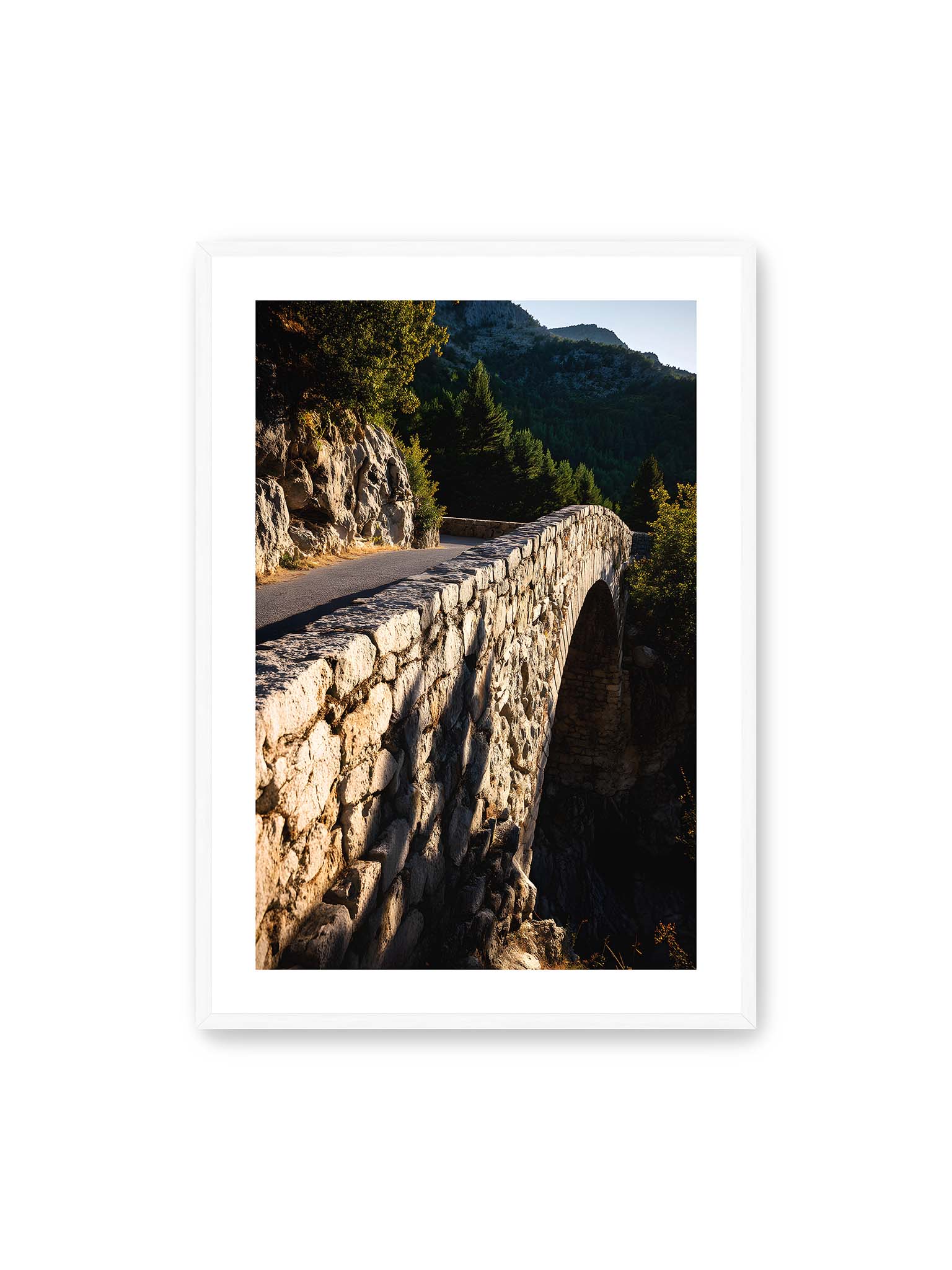 70x100 cm, weißer Galerie-Rand, weißer Rahmen – Steinbrücke mit architektonischem Bogen, beleuchtet vom Abendlicht, umrahmt von einer grünen Landschaft.
