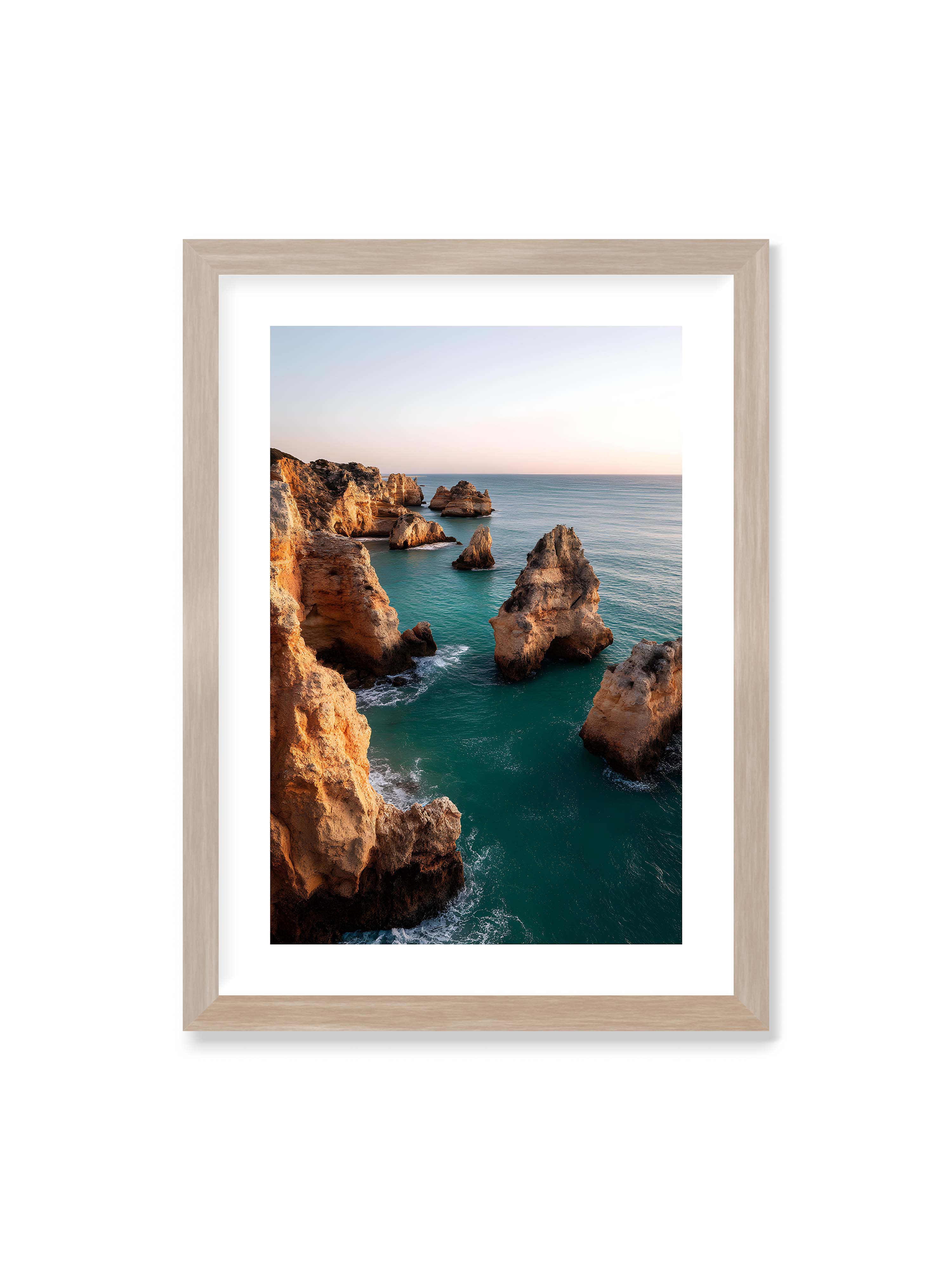 50x70 cm mit weißem Galerie-Rand im Eichenrahmen – Felsformationen an der Küste, umgeben von azurblauem Wasser und goldenem Licht des späten Nachmittags.