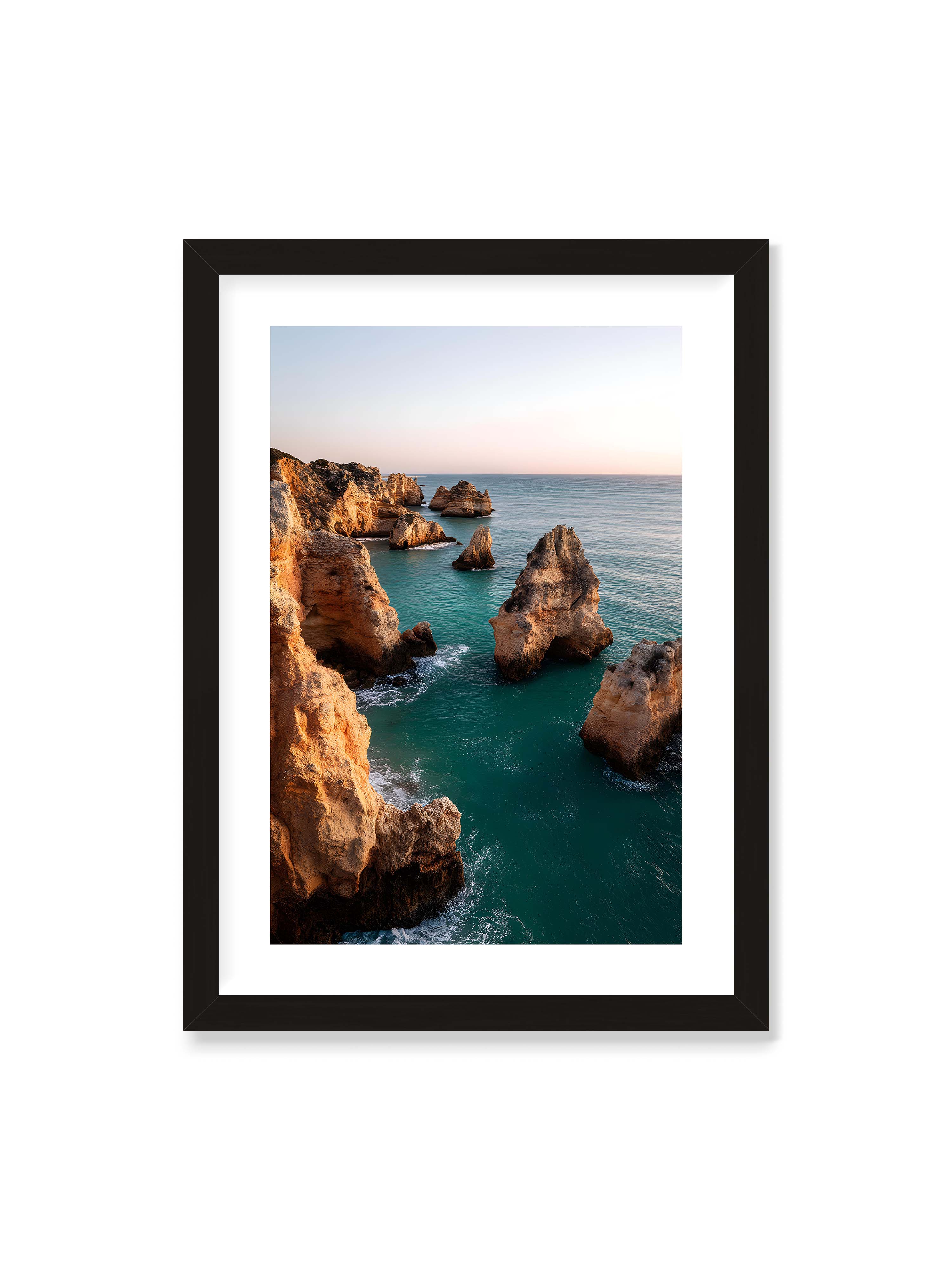 50x70 cm mit weißem Galerie-Rand mit schwarzem Rahmen – Felsformationen an der Küste, umgeben von azurblauem Wasser und goldenem Licht des späten Nachmittags.