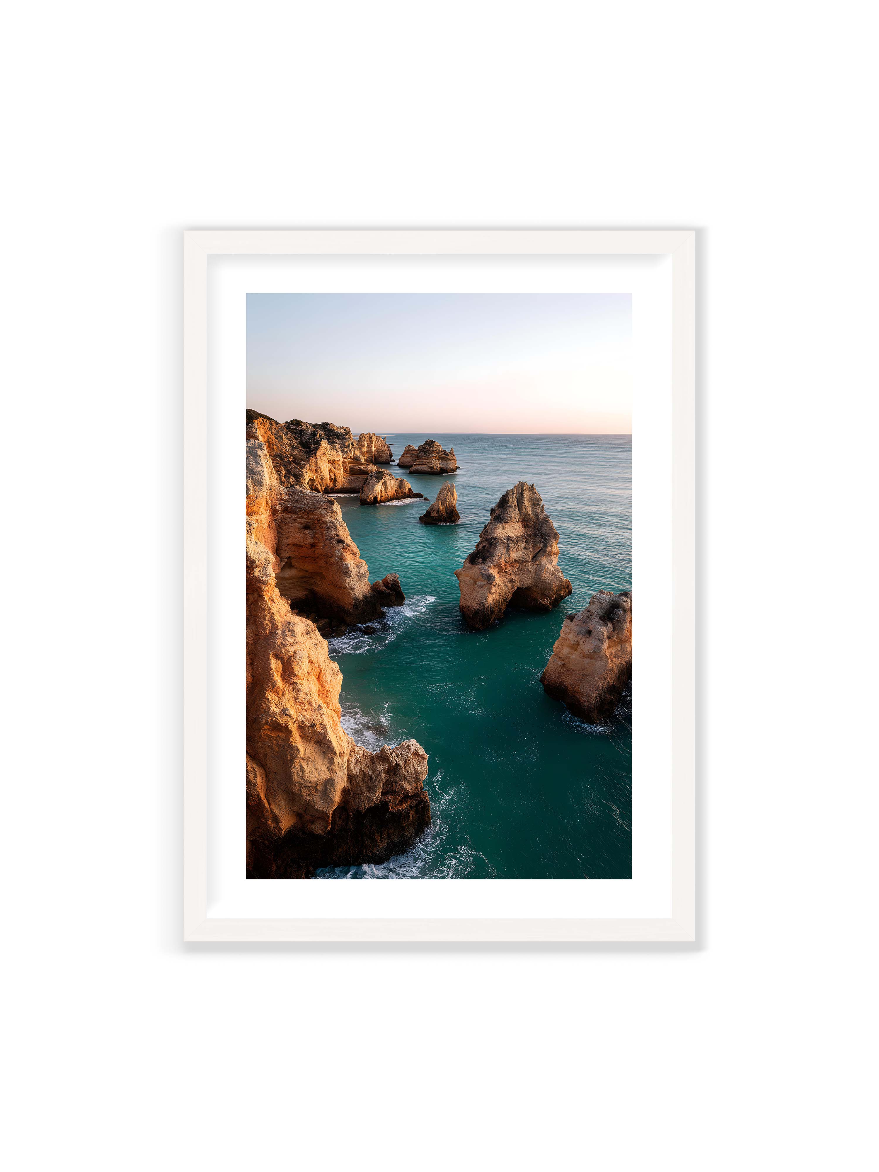 70x100 cm mit weißem Galerie-Rand mit weißem Rahmen – Felsformationen an der Küste, umgeben von azurblauem Wasser und goldenem Licht des späten Nachmittags.