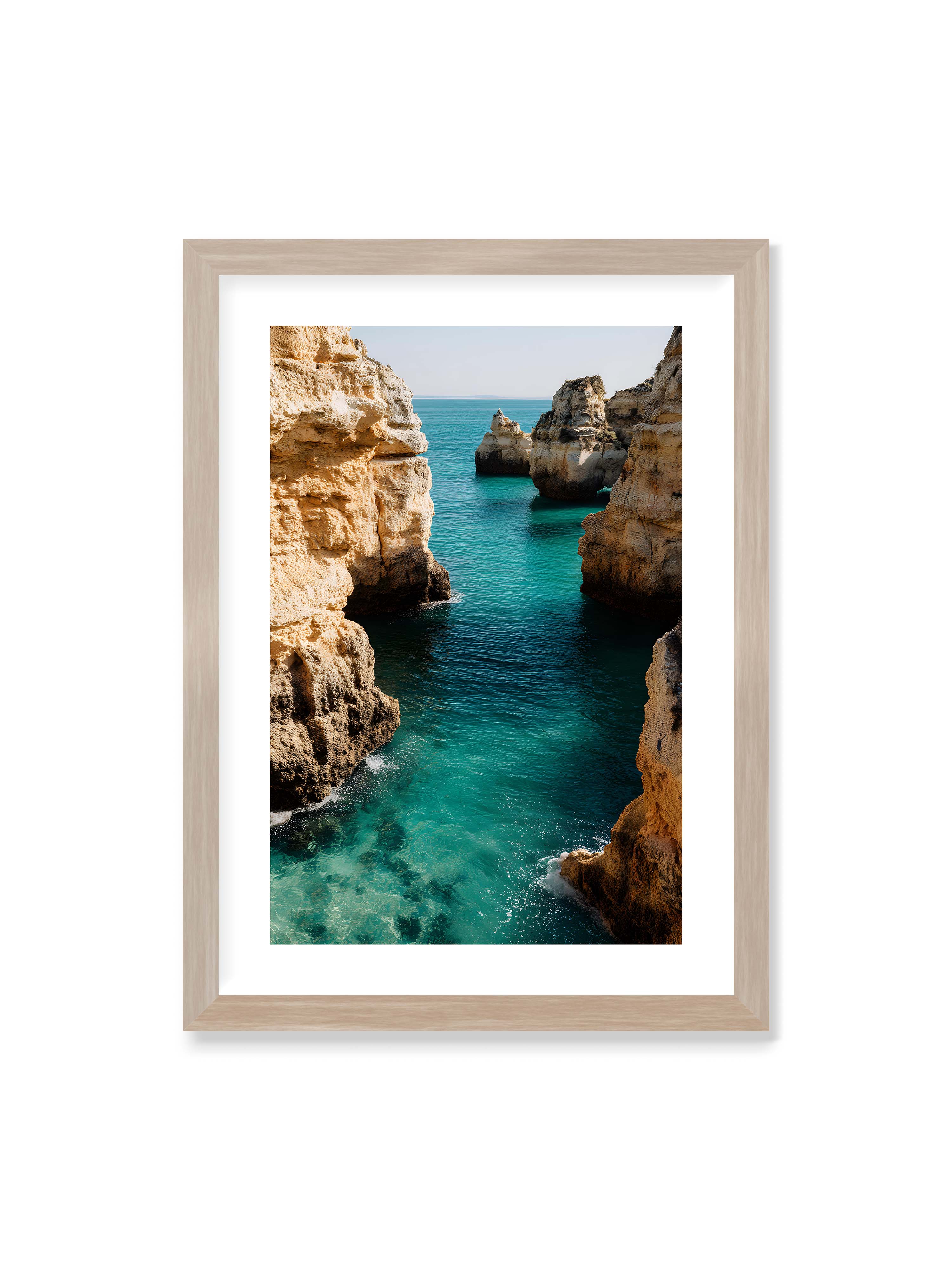 50x70 cm mit weißem Galerie-Rand im Eichenrahmen – Felsen an einer Küste, umgeben von klarem, türkisfarbenem Wasser, das sanft an die Klippen schwappt.