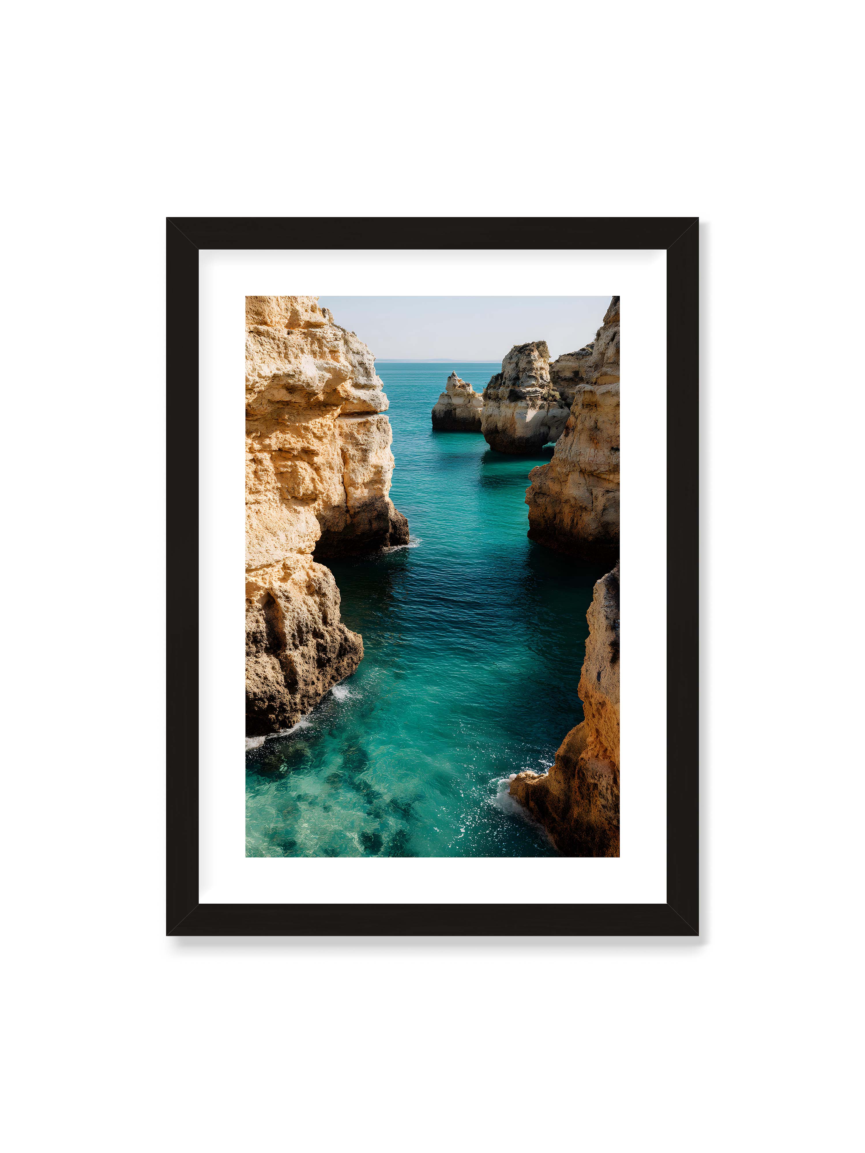 50x70 cm mit weißem Galerie-Rand mit schwarzem Rahmen – Felsen an einer Küste, umgeben von klarem, türkisfarbenem Wasser, das sanft an die Klippen schwappt.