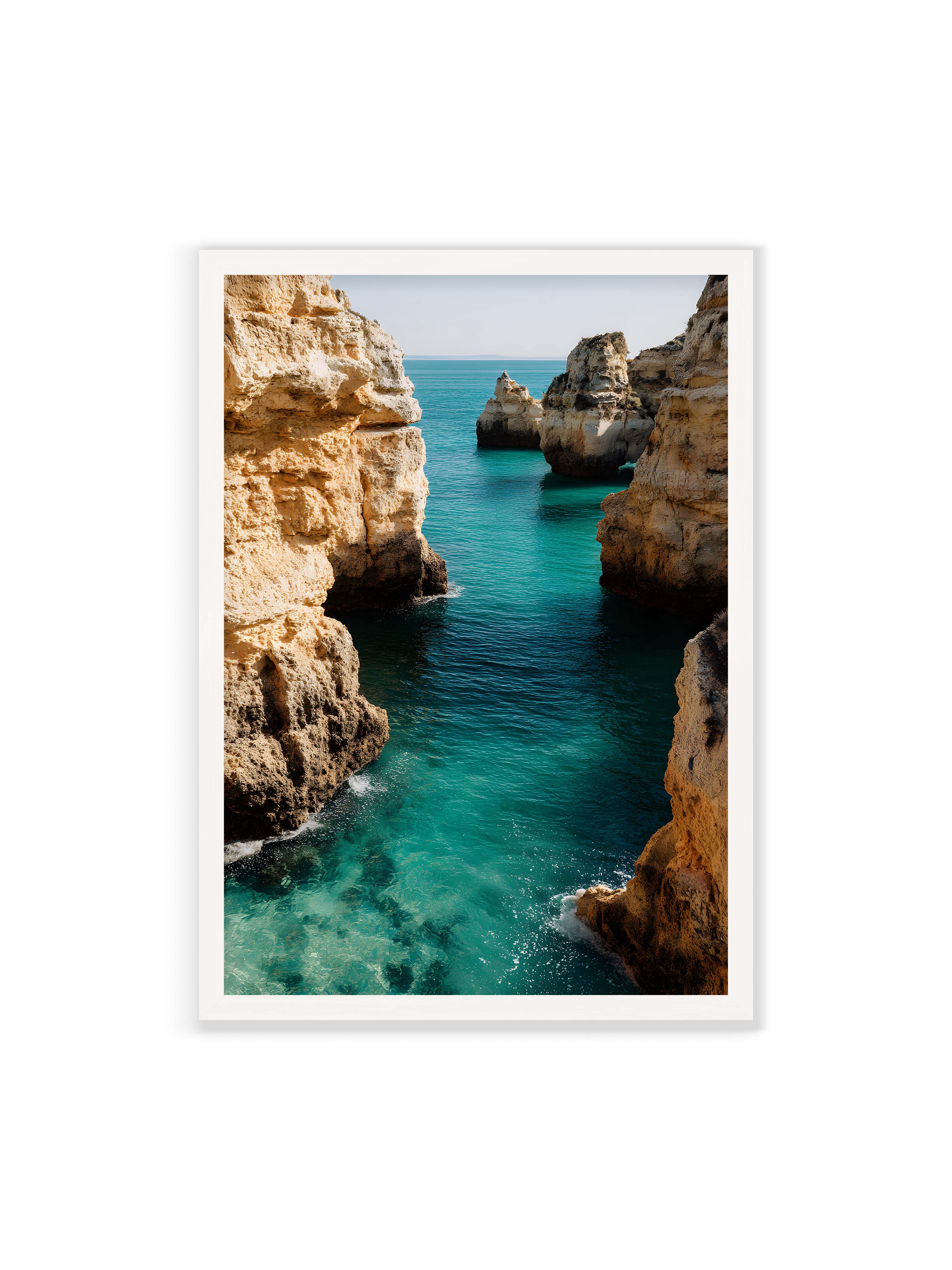 70x100 cm ohne Galerie-Rand mit weißem Rahmen – Felsen an einer Küste, umgeben von klarem, türkisfarbenem Wasser, das sanft an die Klippen schwappt.