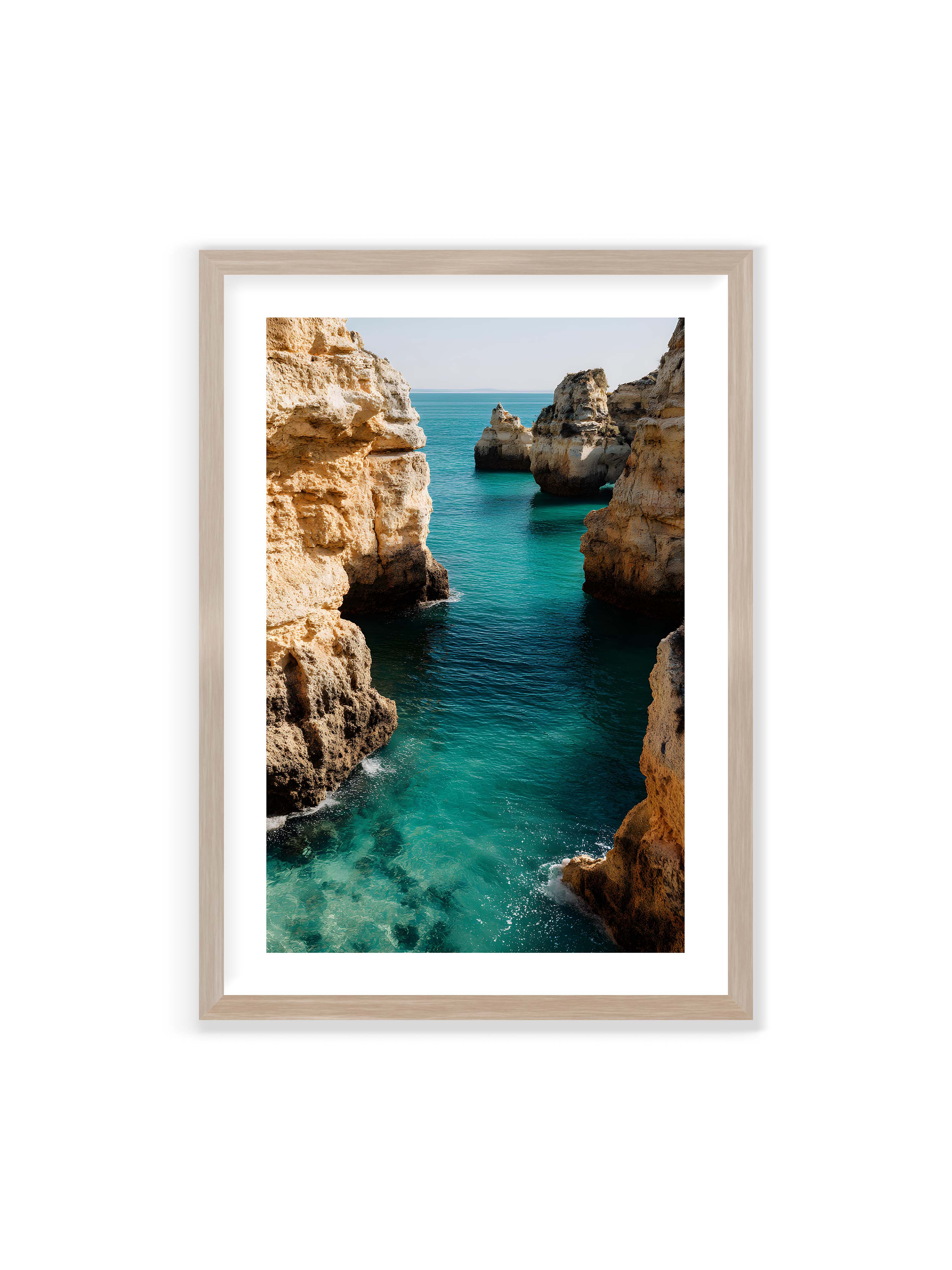 70x100 cm mit weißem Galerie-Rand im Eichenrahmen – Felsen an einer Küste, umgeben von klarem, türkisfarbenem Wasser, das sanft an die Klippen schwappt.