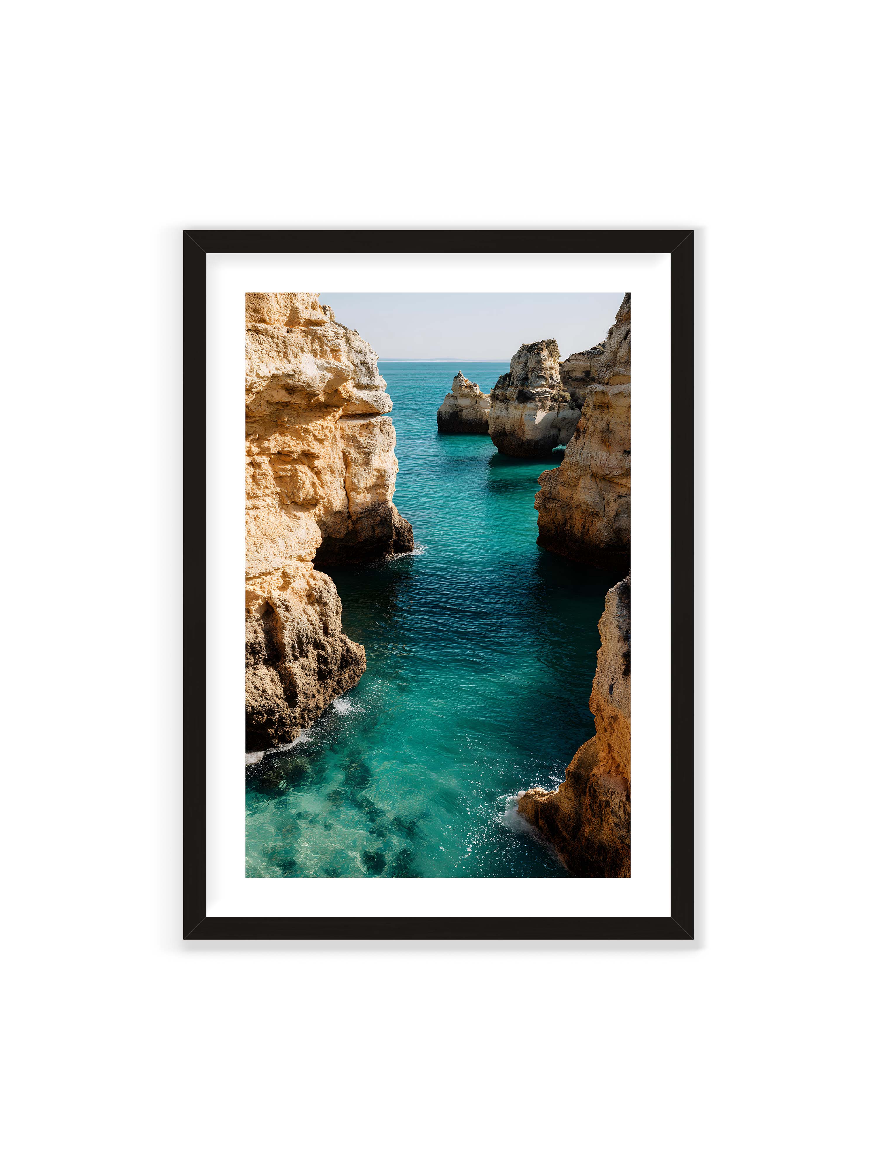 70x100 cm mit weißem Galerie-Rand mit schwarzem Rahmen – Felsen an einer Küste, umgeben von klarem, türkisfarbenem Wasser, das sanft an die Klippen schwappt.