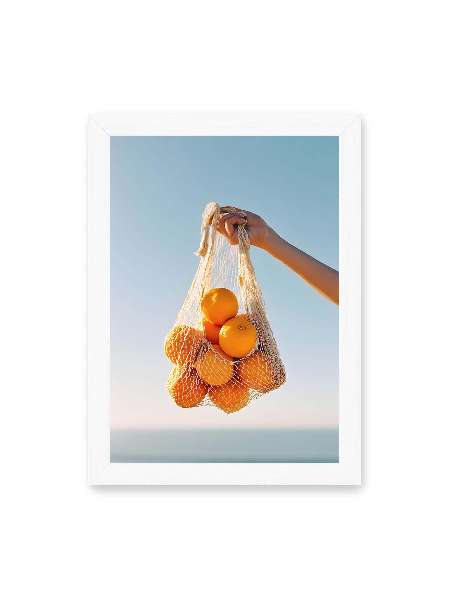 21x30 cm, weißer Rahmen – Hand hält Netz mit Orangen vor klarem blauem Himmel mit starkem Farbkontrast.