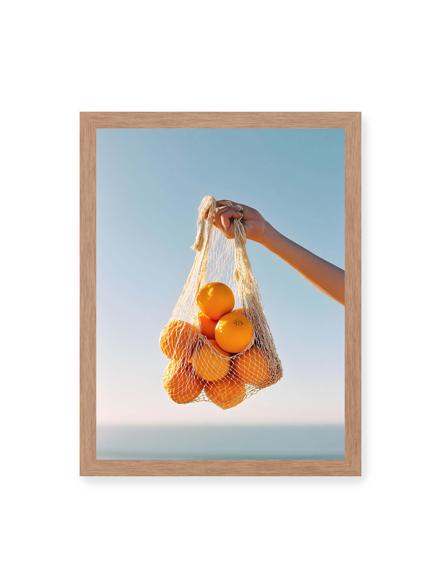 30x40 cm, Eichenrahmen – Hand hält Netz mit Orangen vor klarem blauem Himmel mit starkem Farbkontrast.