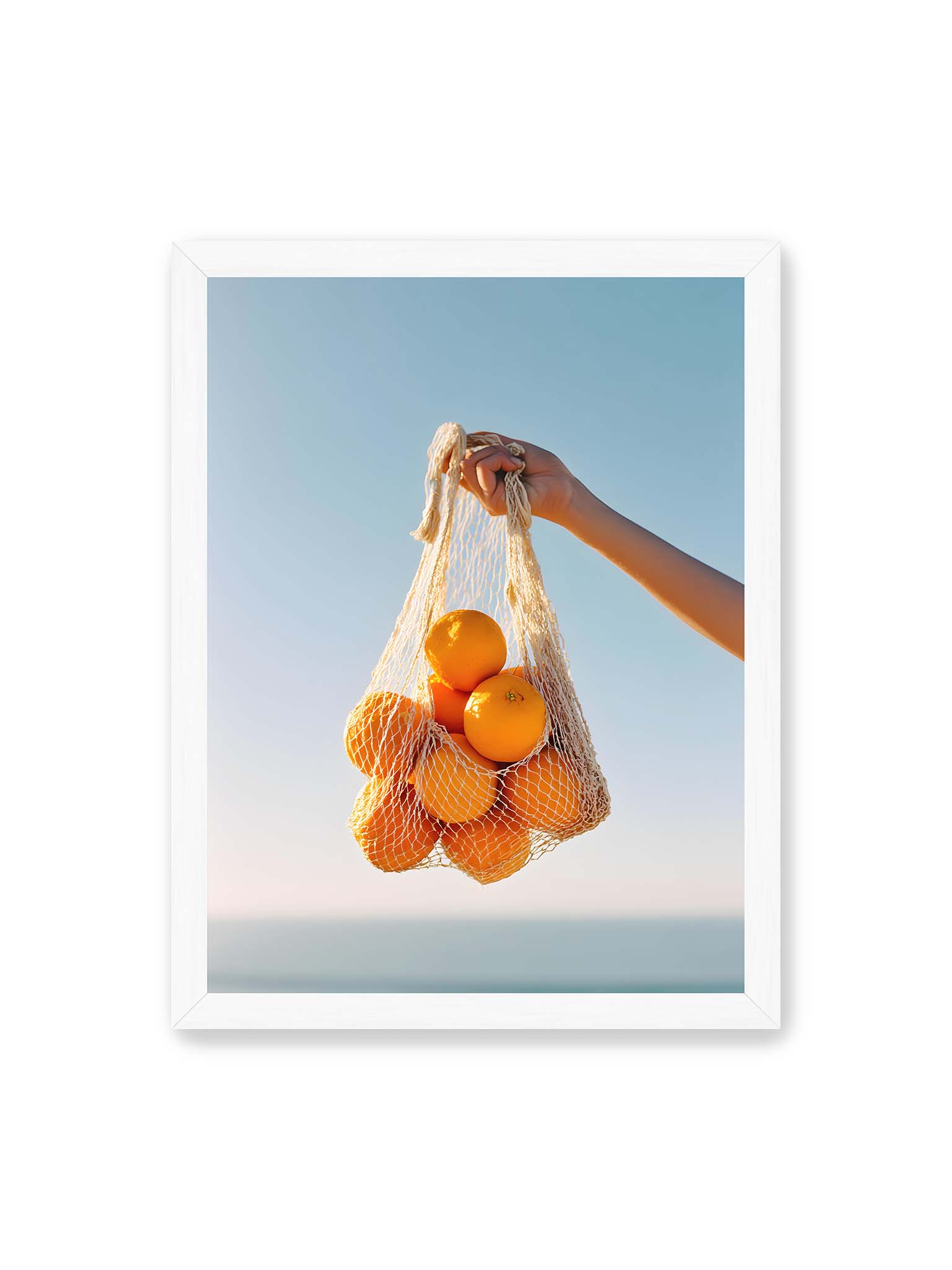 30x40 cm, weißer Rahmen – Hand hält Netz mit Orangen vor klarem blauem Himmel mit starkem Farbkontrast.