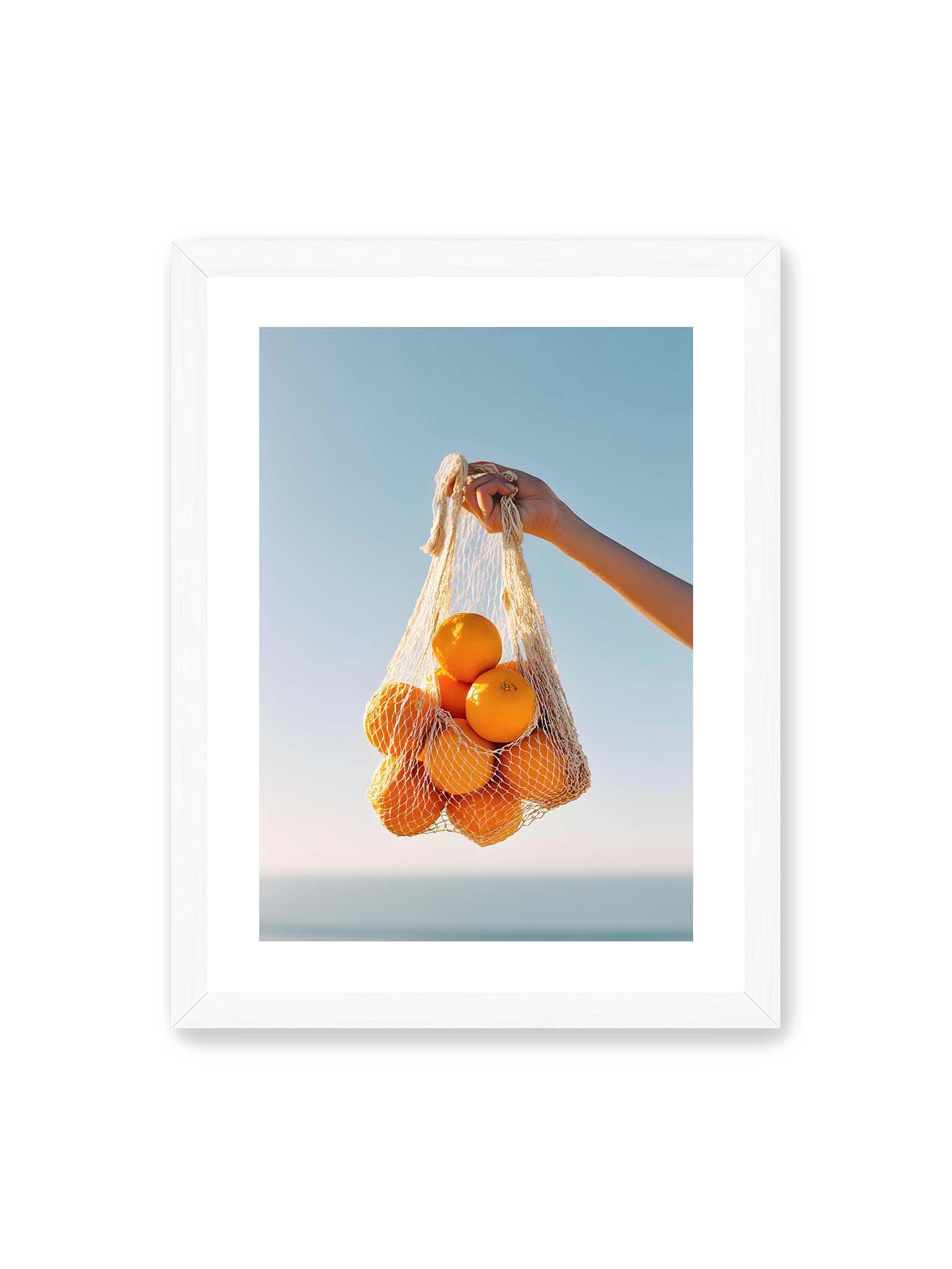 30x40 cm, weißer Galerie-Rand, weißer Rahmen – Hand hält Netz mit Orangen vor klarem blauem Himmel mit starkem Farbkontrast.