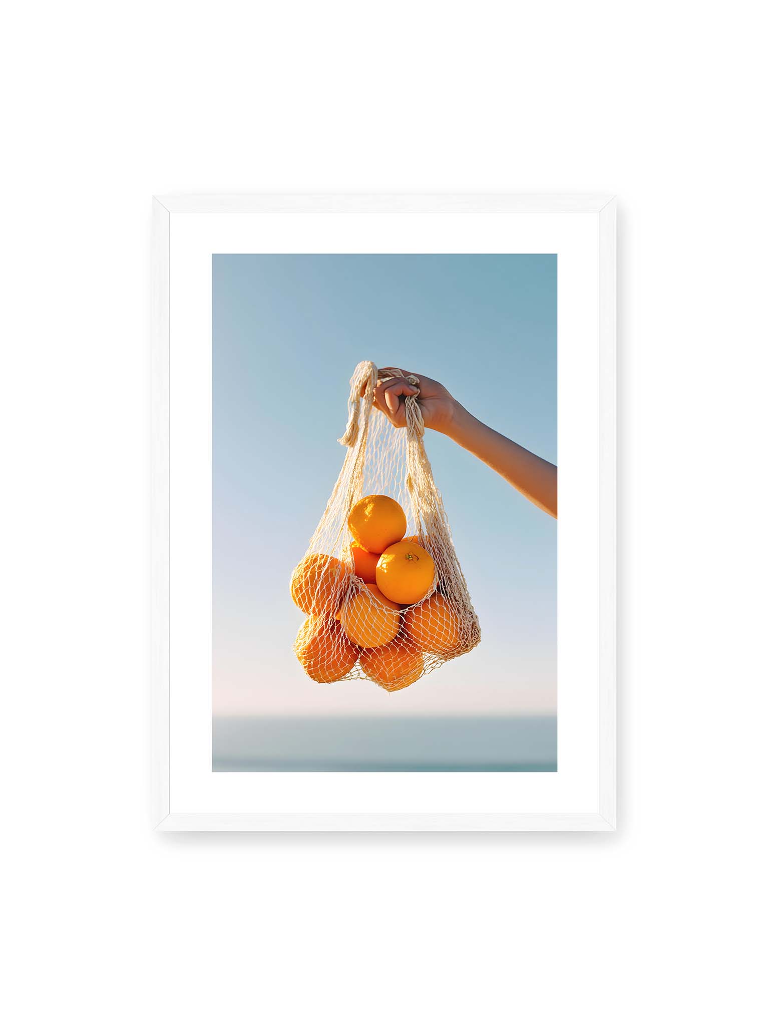 50x70 cm, weißer Galerie-Rand, weißer Rahmen – Hand hält Netz mit Orangen vor klarem blauem Himmel mit starkem Farbkontrast.