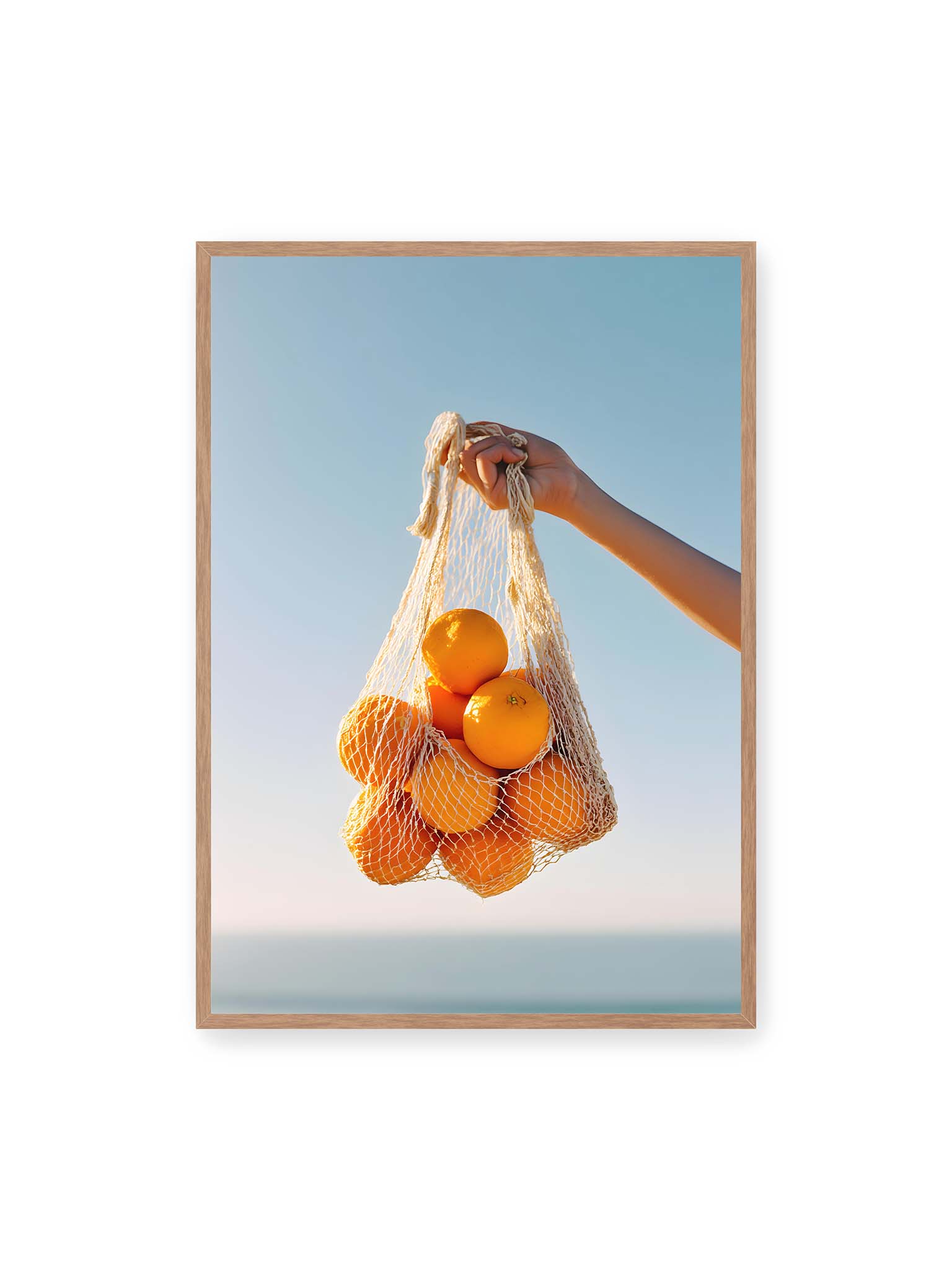 70x100 cm, Eichenrahmen – Hand hält Netz mit Orangen vor klarem blauem Himmel mit starkem Farbkontrast.