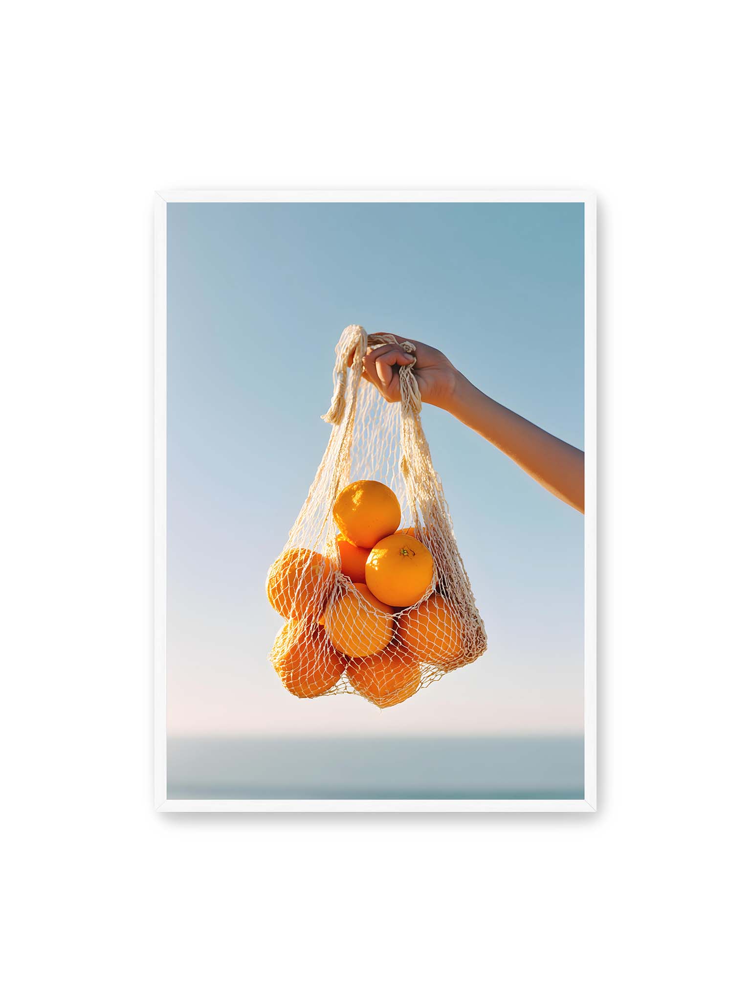 70x100 cm, weißer Rahmen – Hand hält Netz mit Orangen vor klarem blauem Himmel mit starkem Farbkontrast.