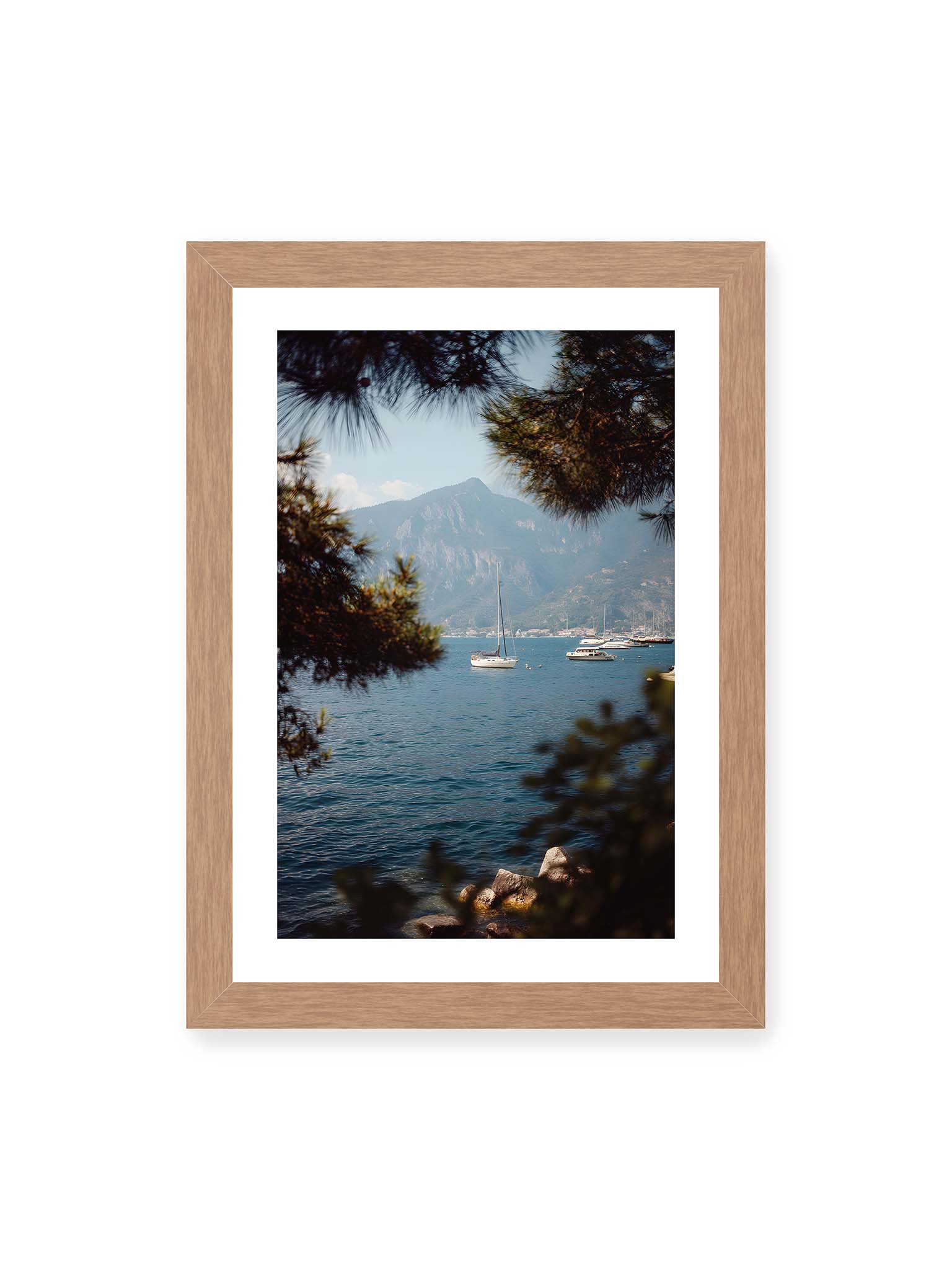 21x30 cm, weißer Galerie-Rand, Eichenrahmen – Segelboote im ruhigen Wasser vor Bergen, eingerahmt von unscharfen Ästen im Vordergrund.