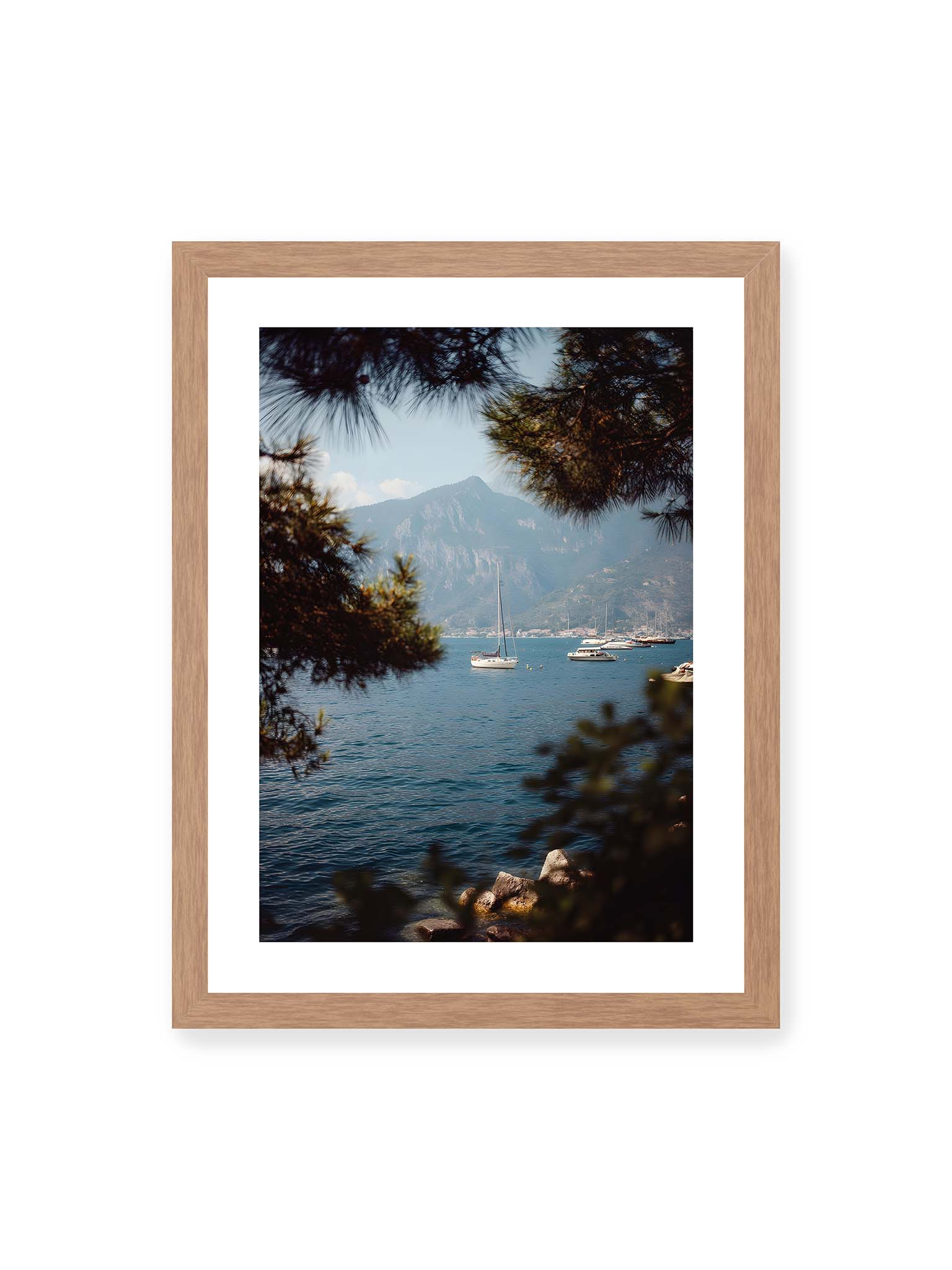 30x40 cm, weißer Galerie-Rand, Eichenrahmen – Segelboote im ruhigen Wasser vor Bergen, eingerahmt von unscharfen Ästen im Vordergrund.