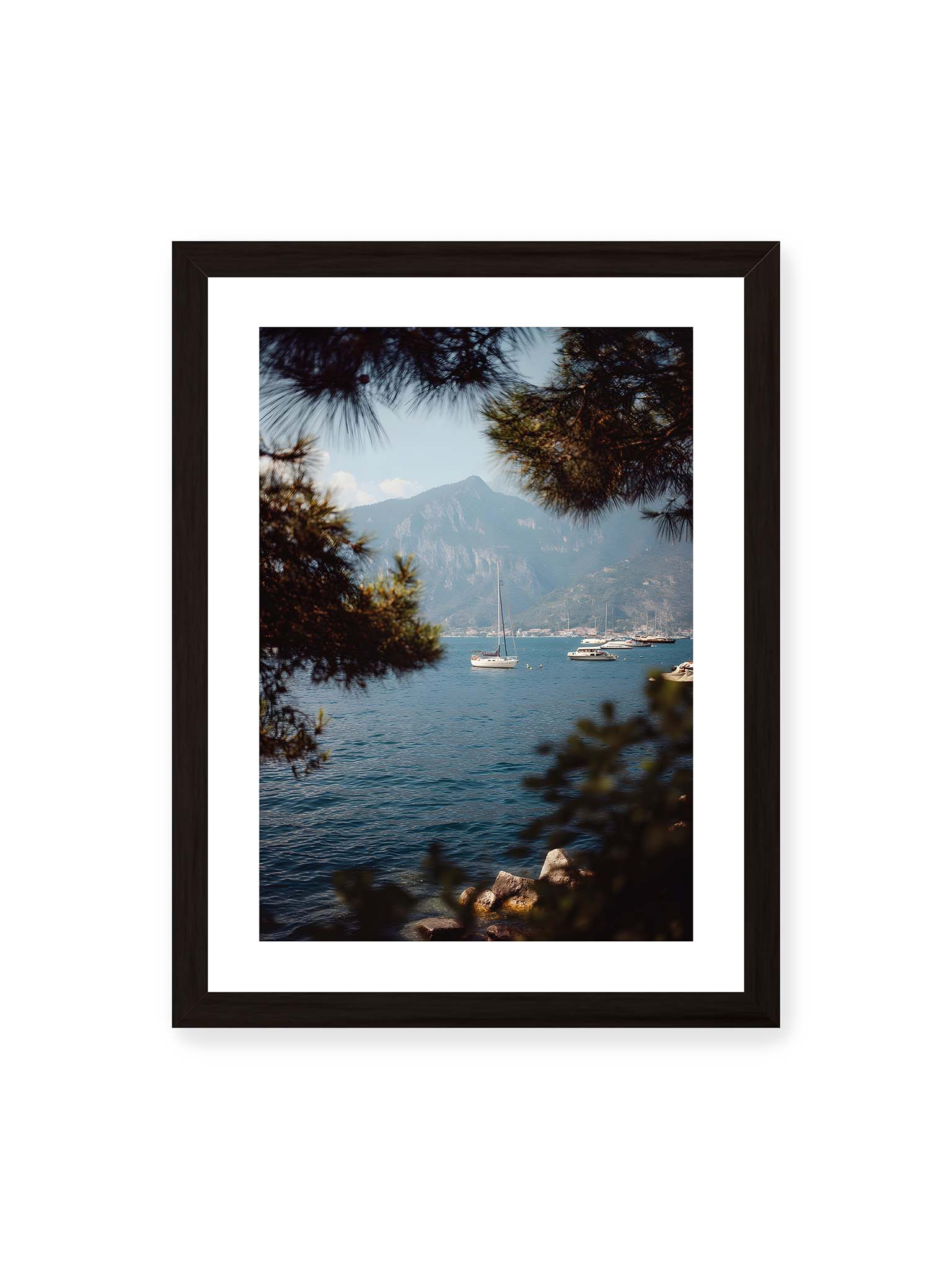 30x40 cm, weißer Galerie-Rand, schwarzer Rahmen – Segelboote im ruhigen Wasser vor Bergen, eingerahmt von unscharfen Ästen im Vordergrund.