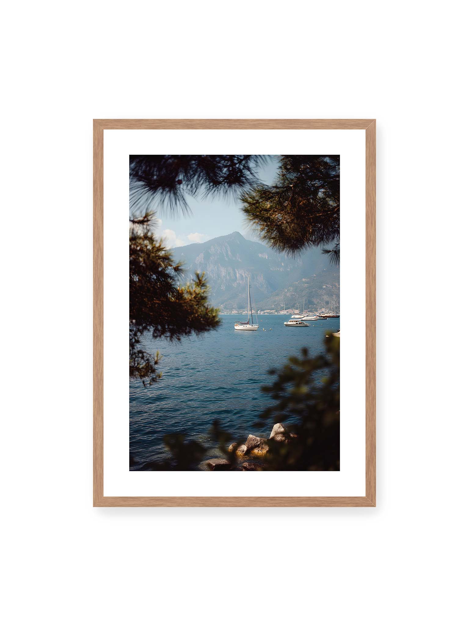 50x70 cm, weißer Galerie-Rand, Eichenrahmen – Segelboote im ruhigen Wasser vor Bergen, eingerahmt von unscharfen Ästen im Vordergrund.